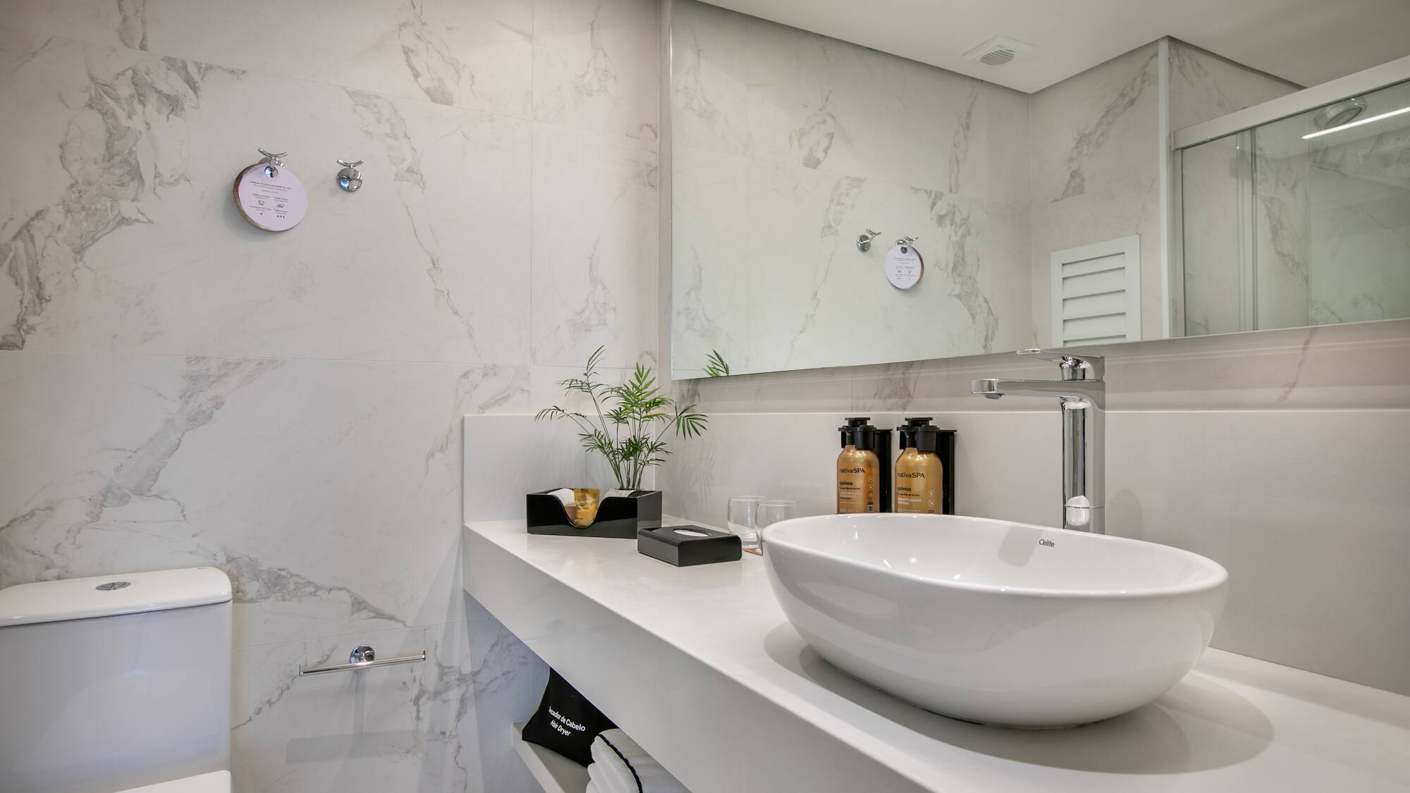 Modern hotel bathroom with white marble walls, vessel sink, and chrome faucet.