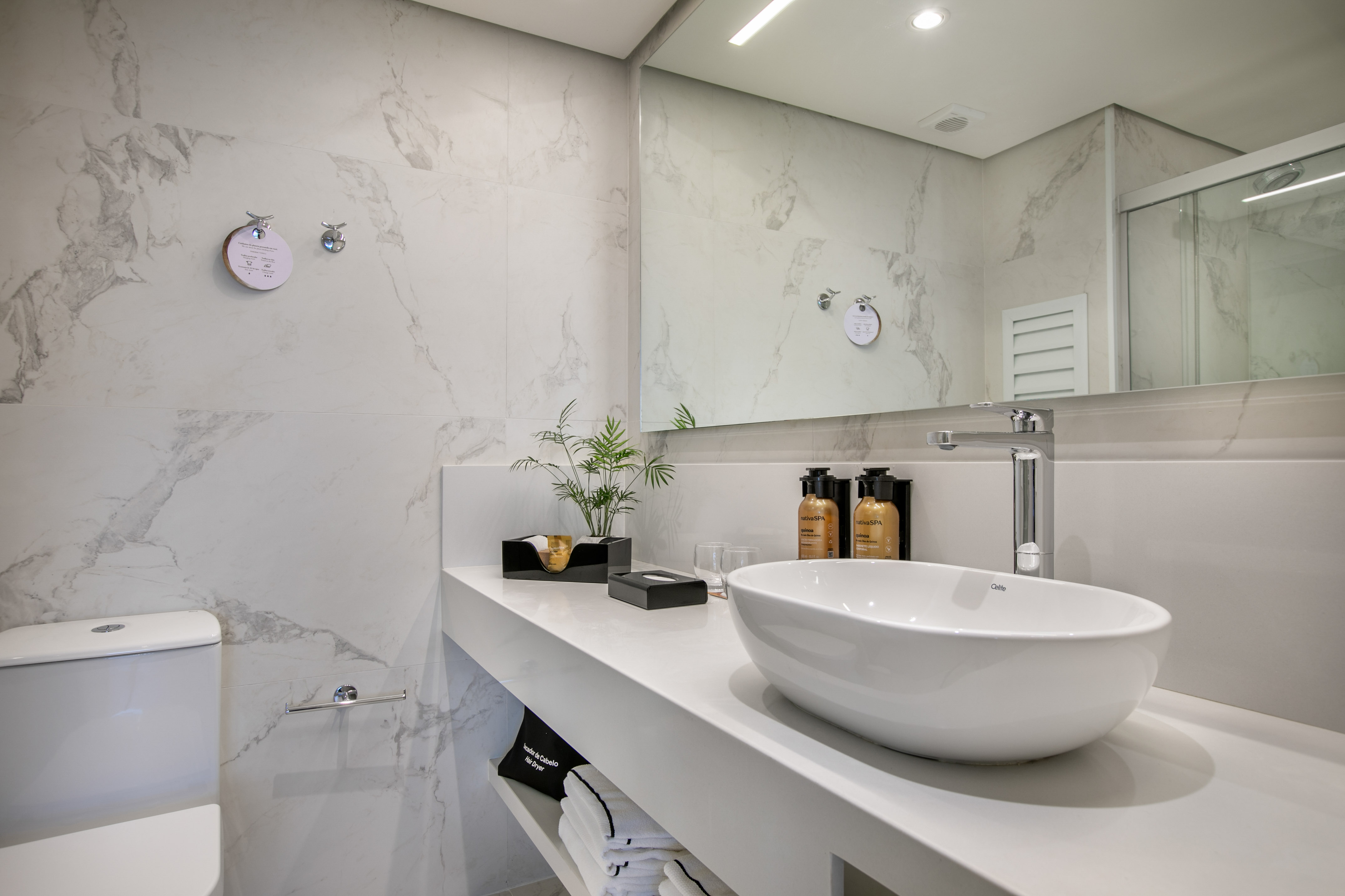 Modern white marble bathroom with vanity, oval sink, and large mirror.