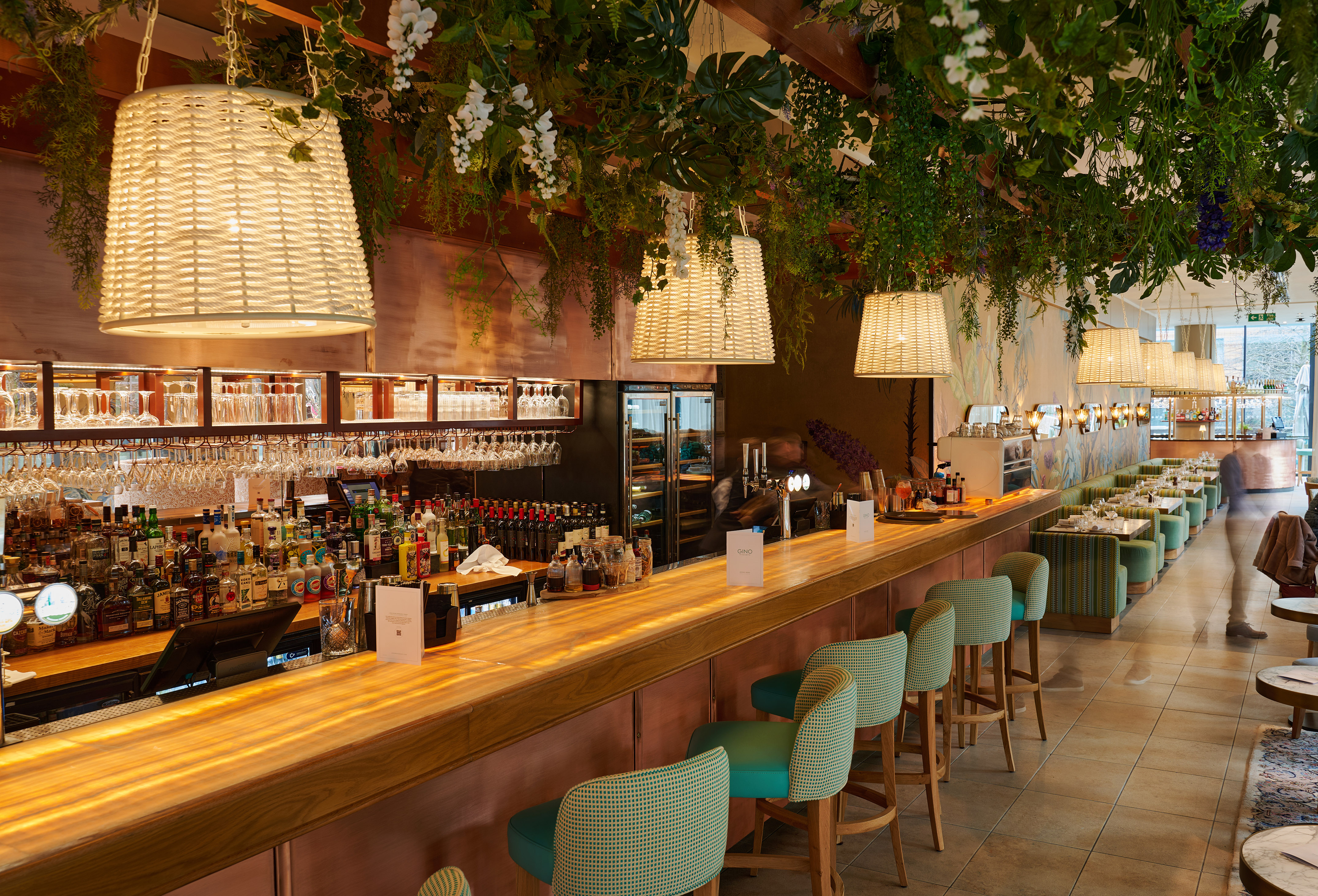 Modern bar with lush greenery, woven pendant lights, and teal bar stools.