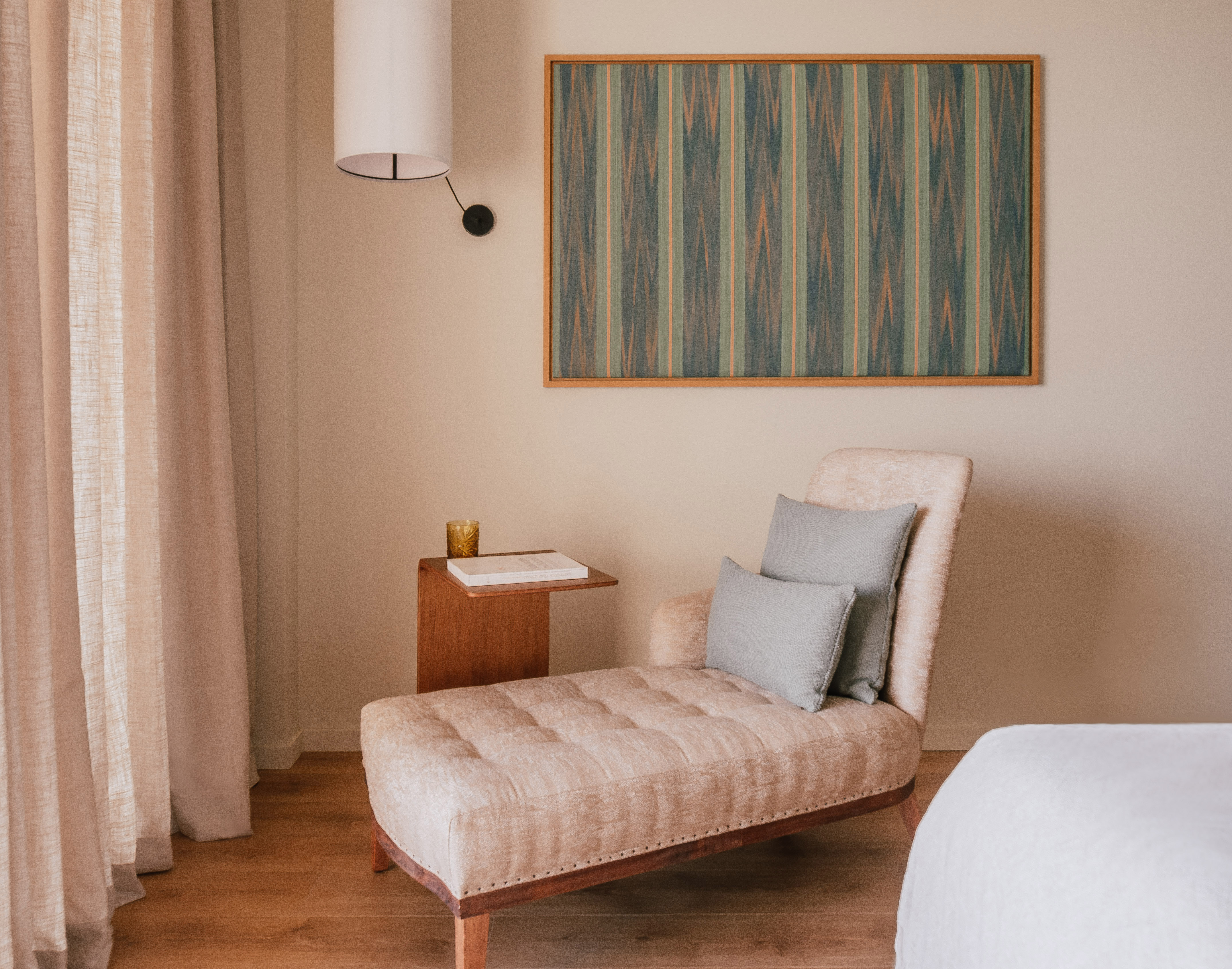 Beige tufted chaise lounge, wood table, abstract striped wall art, and lamp.