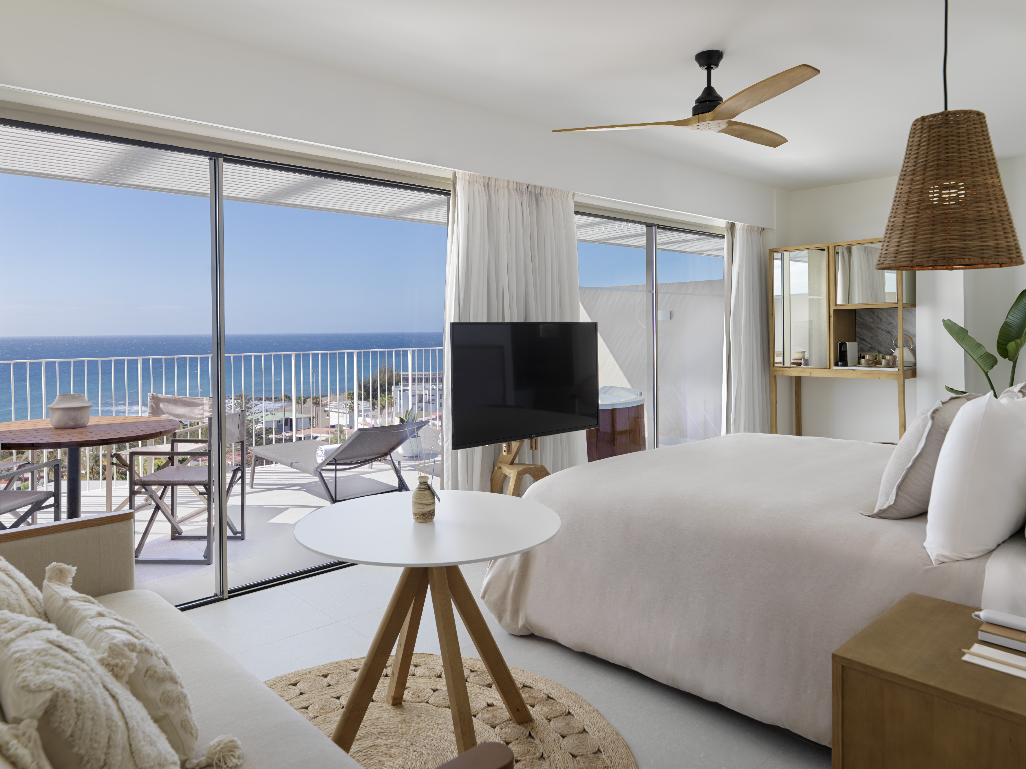 Modern resort bedroom with ocean view balcony, large bed, and outdoor seating.