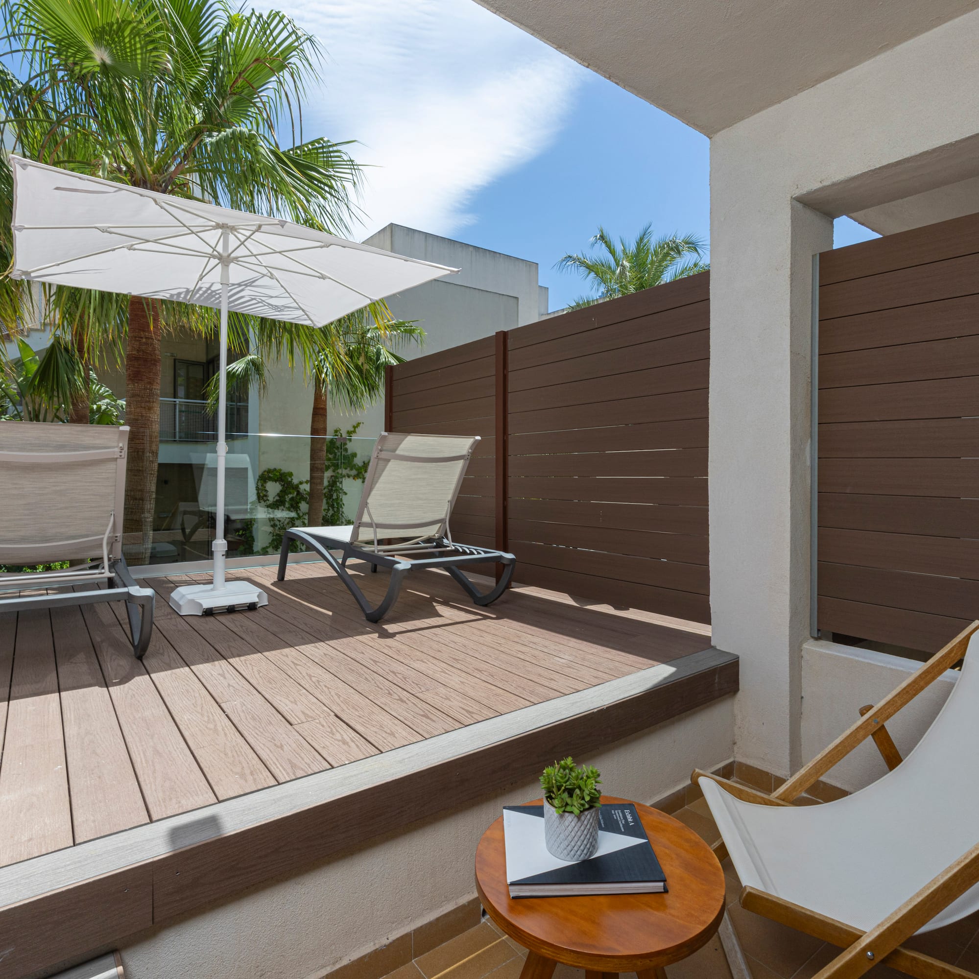 Modern balcony deck with sun loungers, umbrella, and privacy fence.