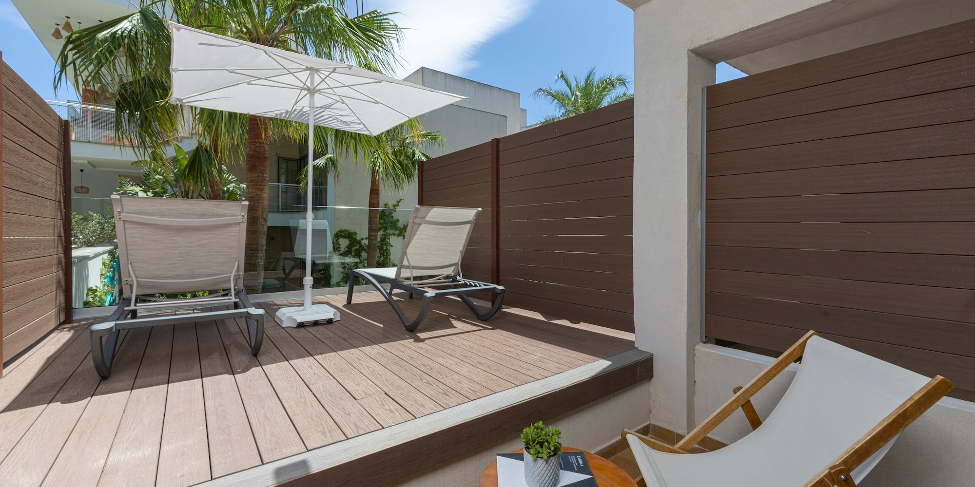 Modern balcony deck with sun loungers, umbrella, and privacy fence.