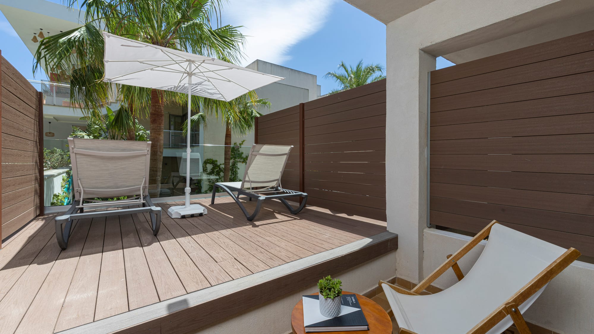 Modern balcony deck with sun loungers, umbrella, and privacy fence.