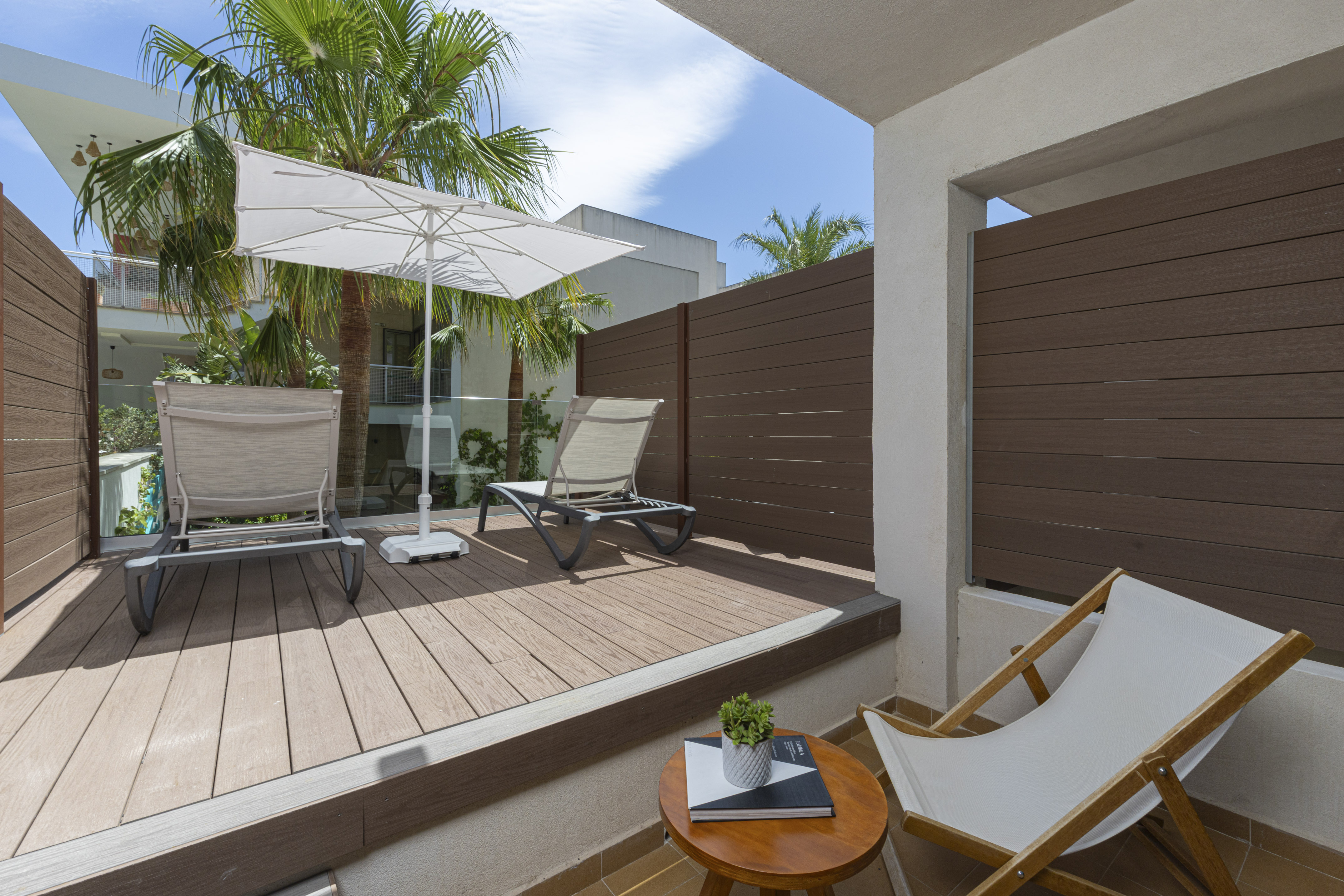 Modern balcony deck with sun loungers, umbrella, and privacy fence.
