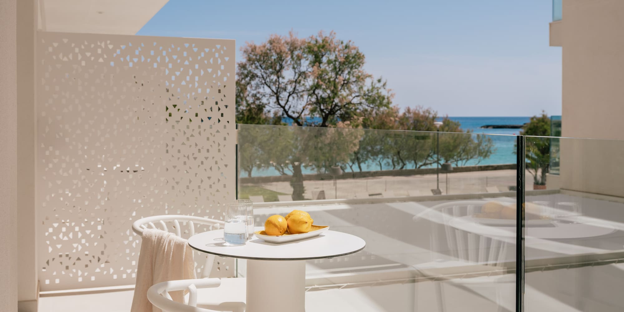 White hotel balcony with lemons, water, and clear blue sea view.