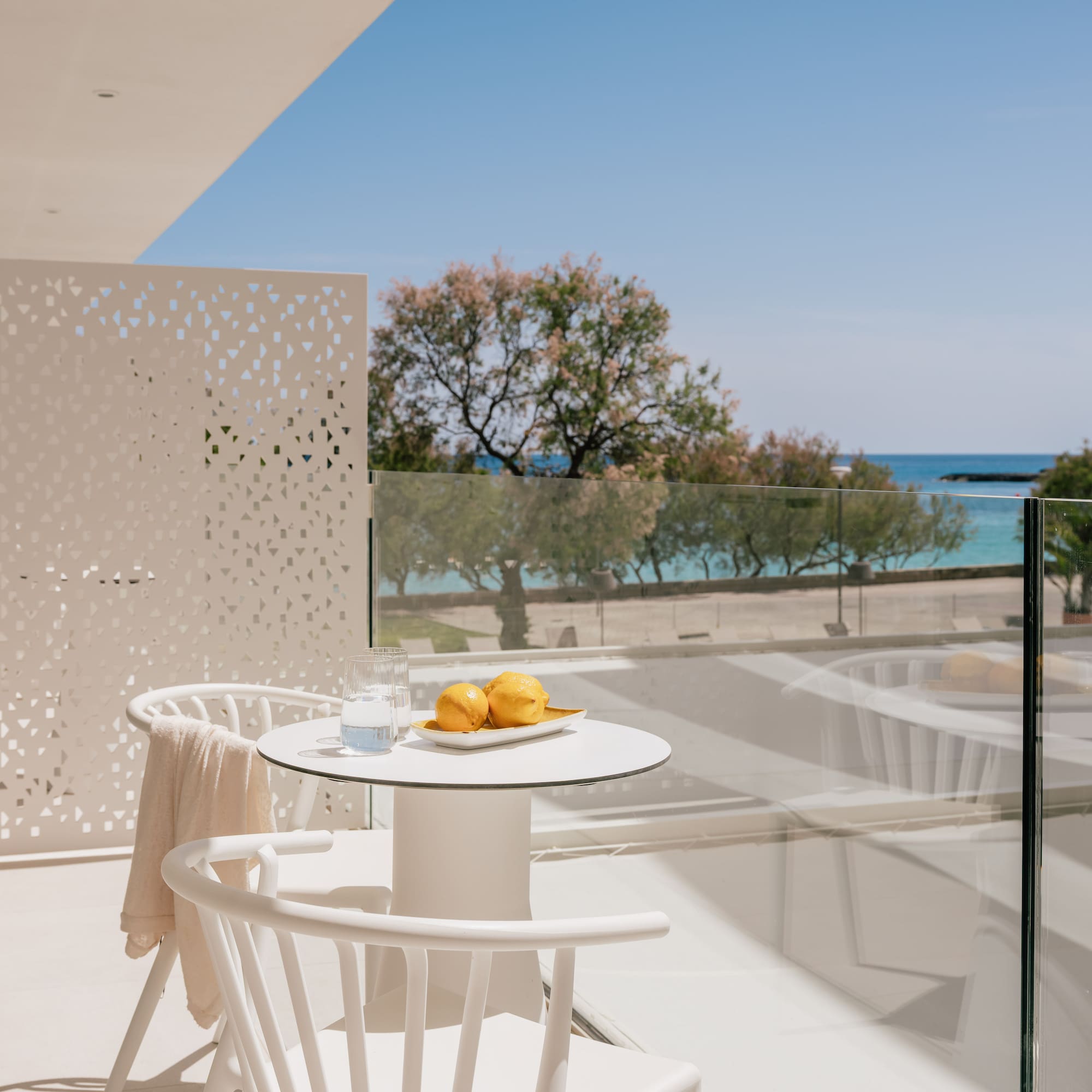 White hotel balcony with lemons, water, and clear blue sea view.