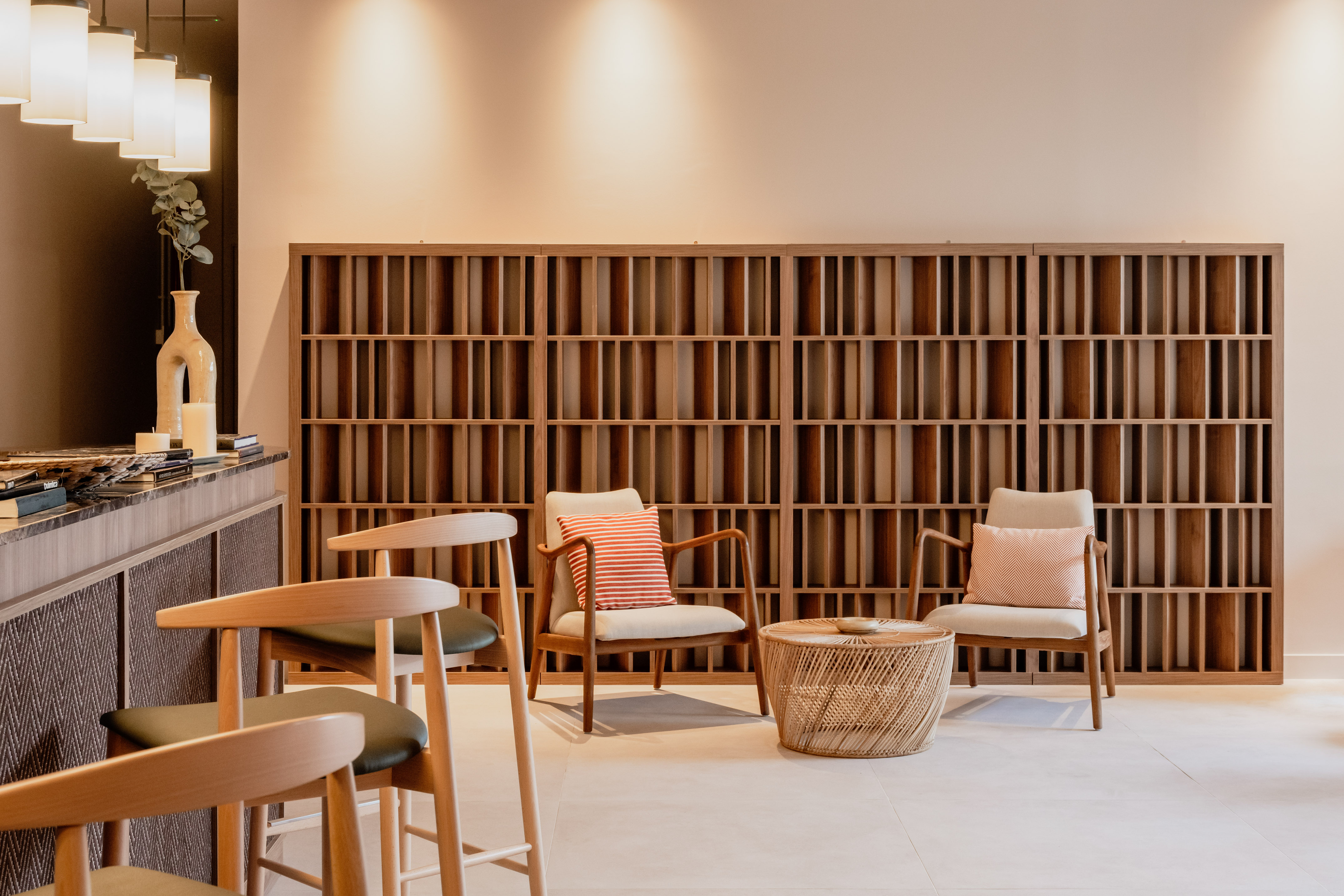 Contemporary lounge with wooden slatted shelving, armchairs, and rattan coffee table.