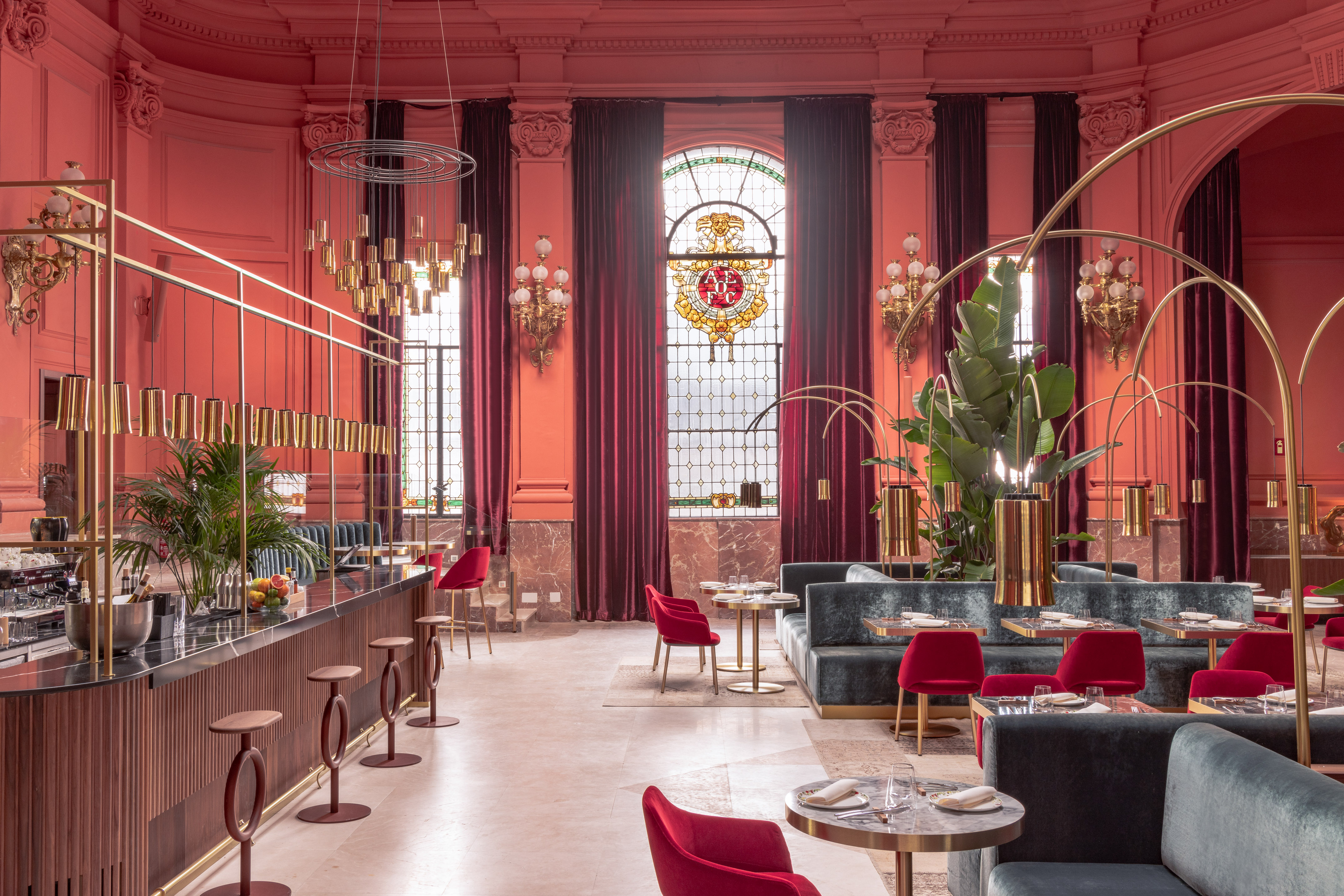 Luxurious coral restaurant interior with gold accents, velvet seating, and stained glass.