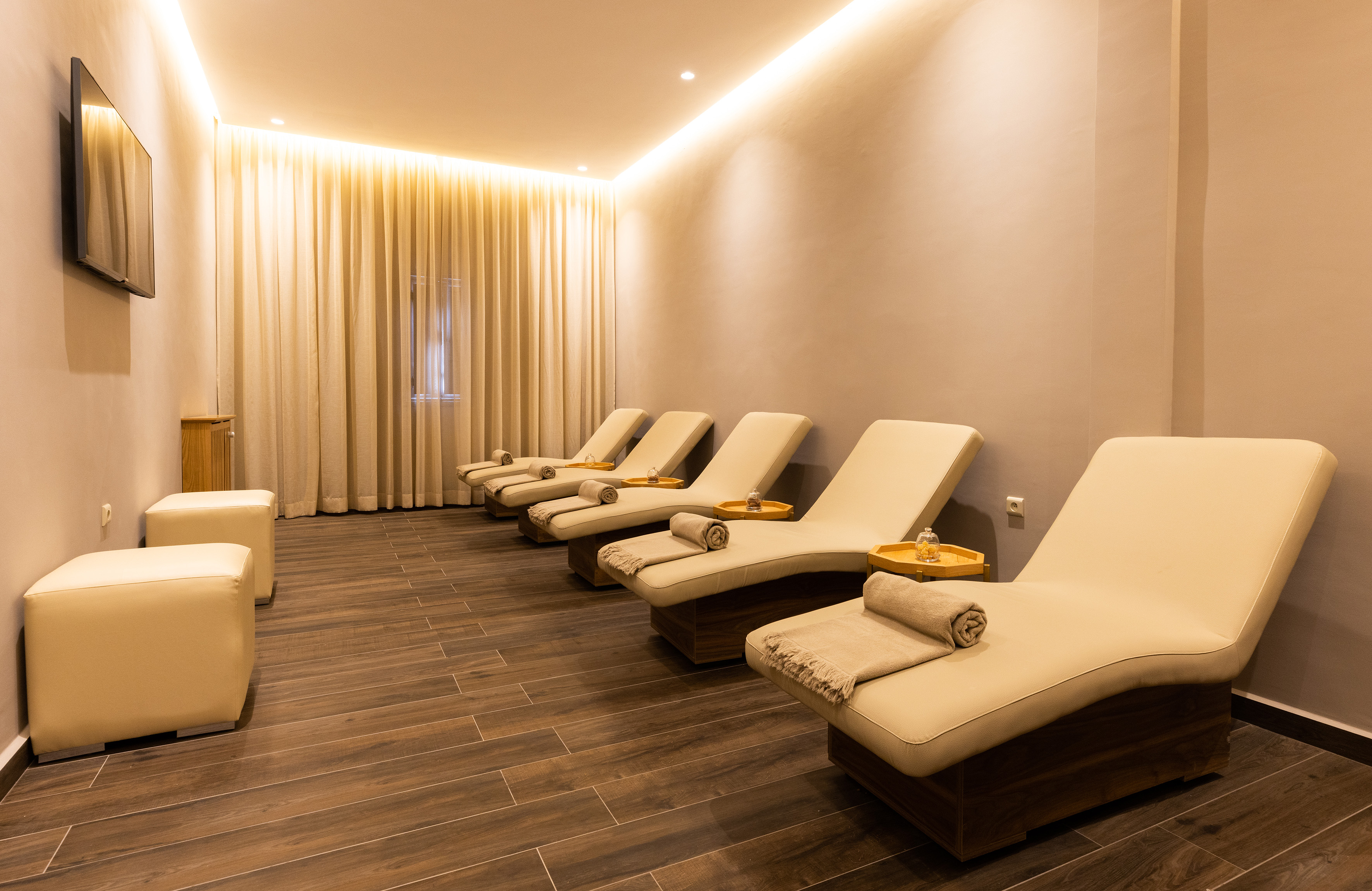 Spa relaxation room with beige loungers, warm lighting, and wood floor.