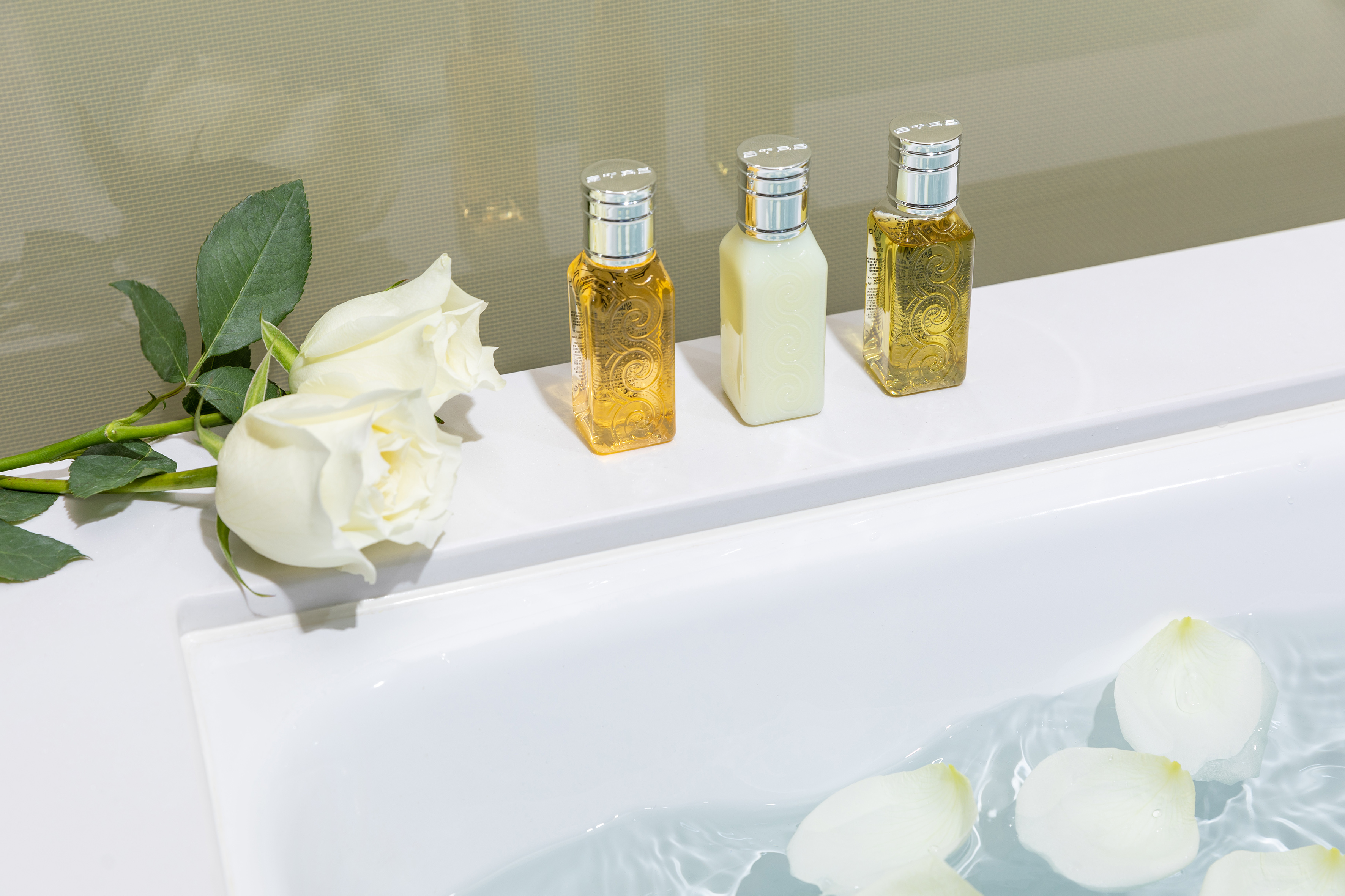 Spa bath with white roses, floating petals, and hotel amenity bottles.