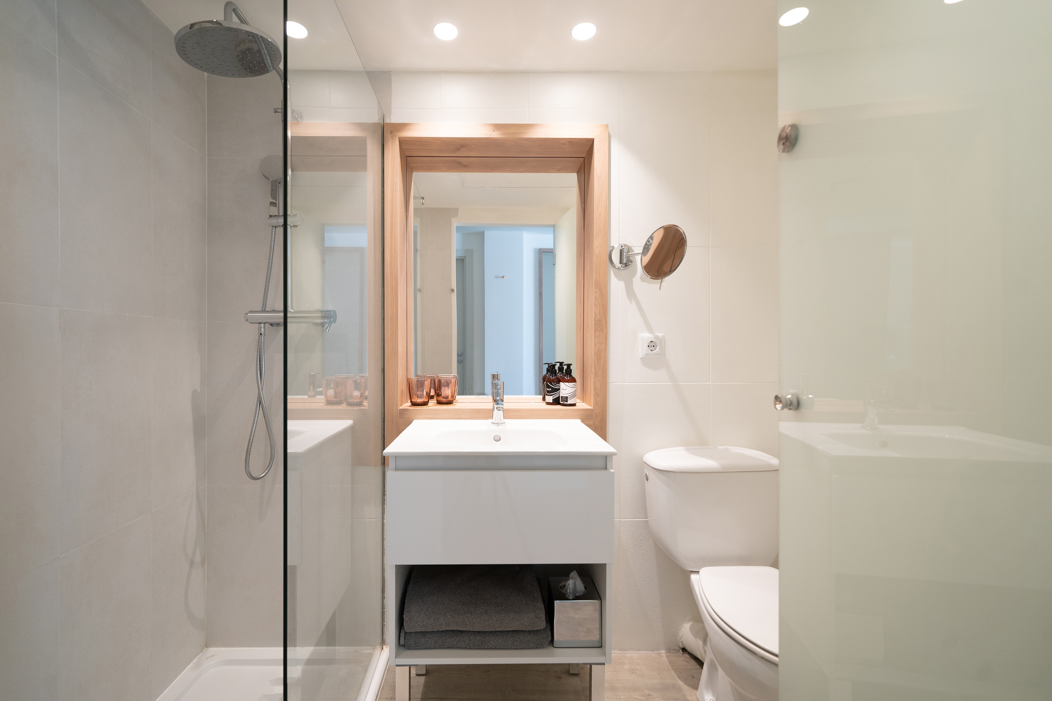 Modern bathroom with glass shower, wooden mirror, white vanity, and toilet.
