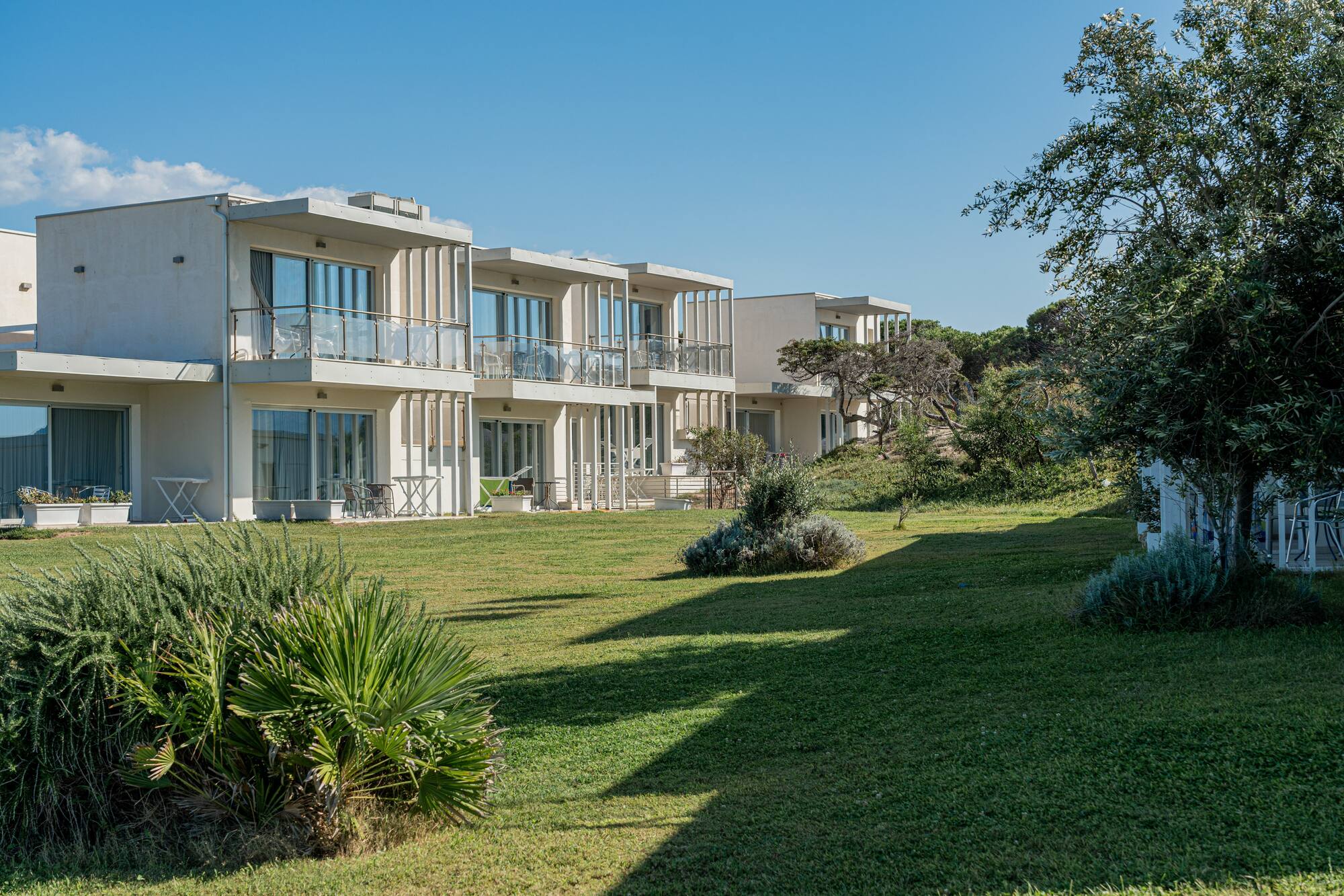 Modern resort apartments with balconies overlooking green lawn and coastal landscaping.