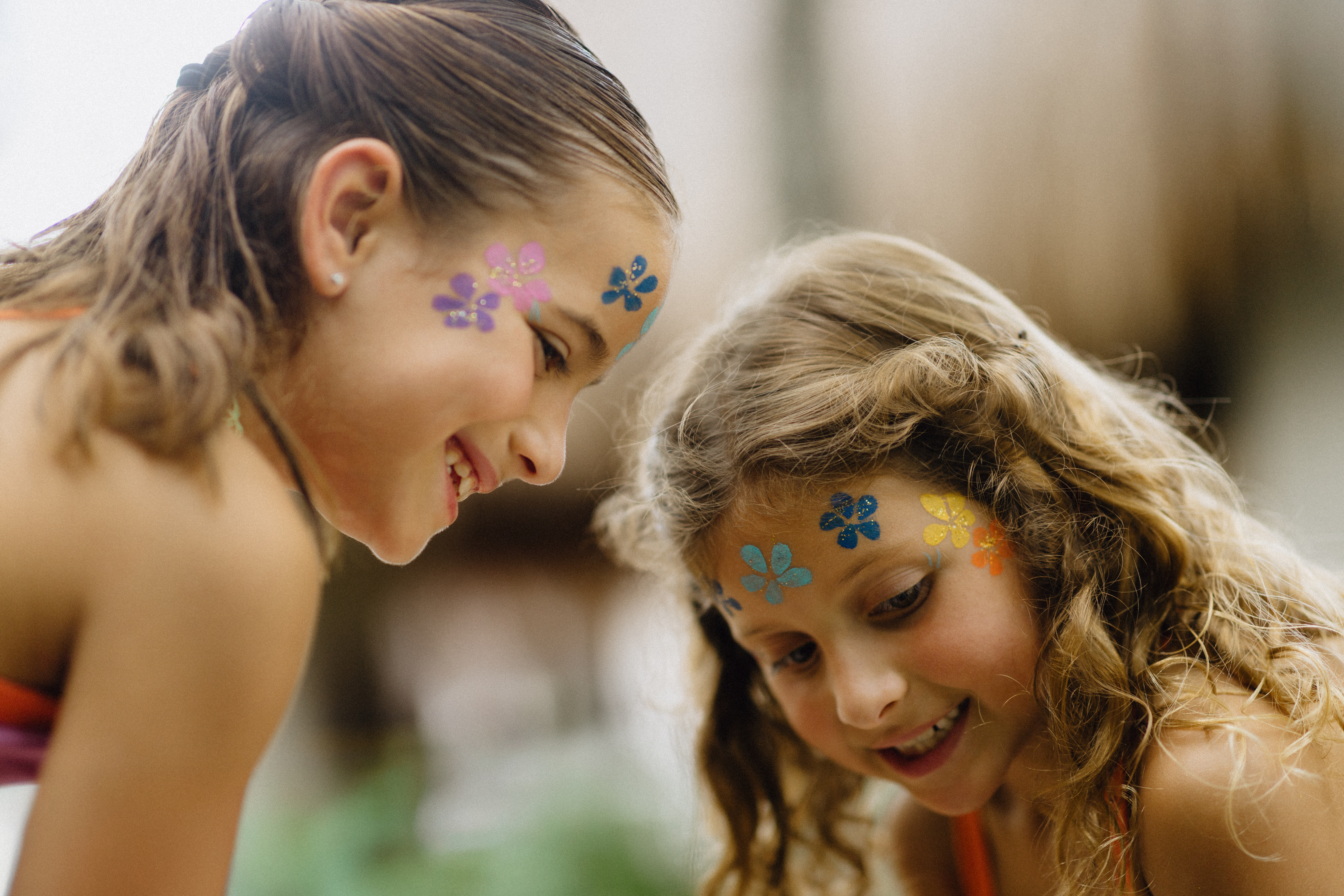 Smiling girls with vibrant glitter flower face paint at a kids party.