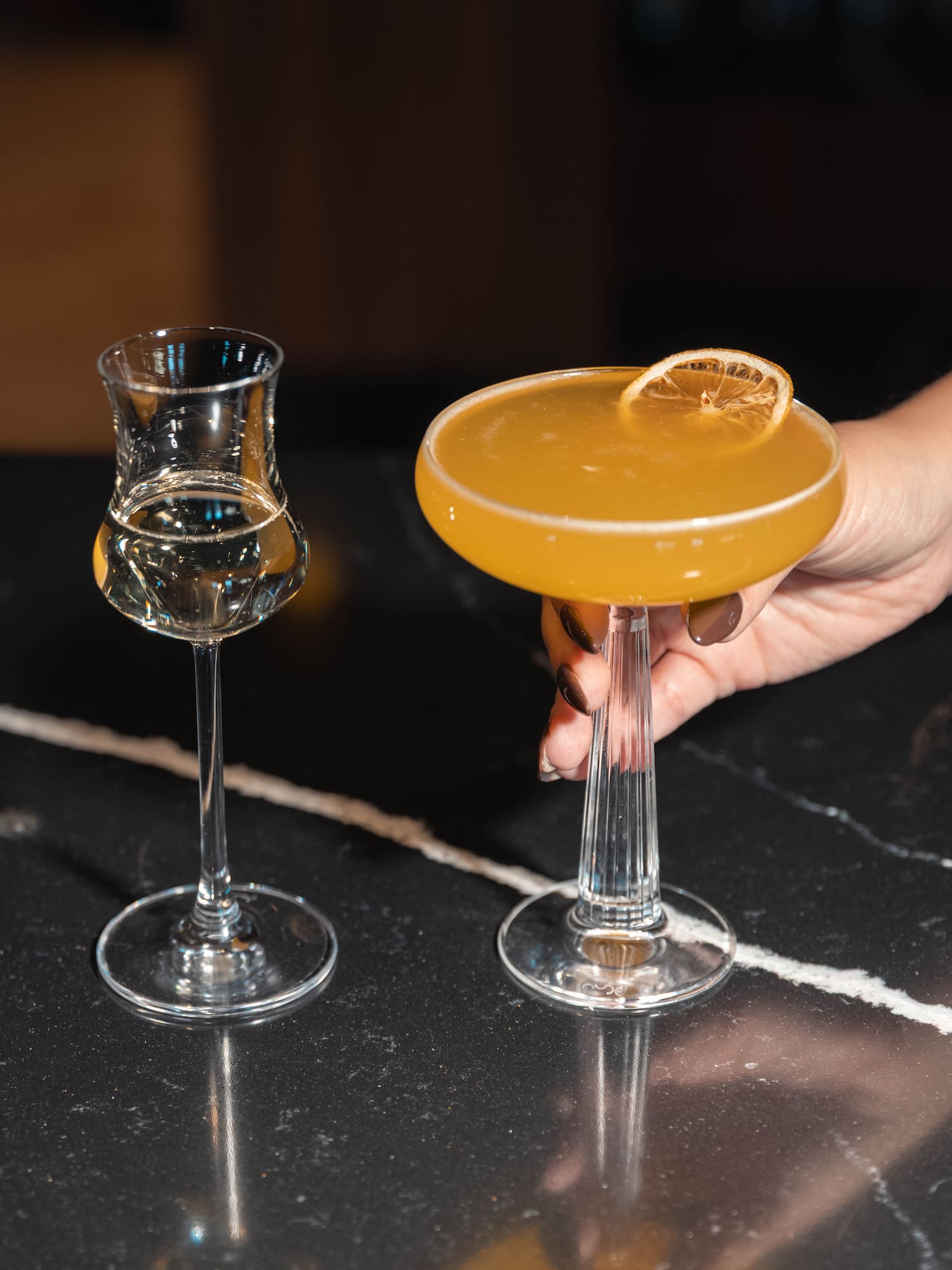 a hand holding a glass of yellow liquid next to a glass of yellow liquid