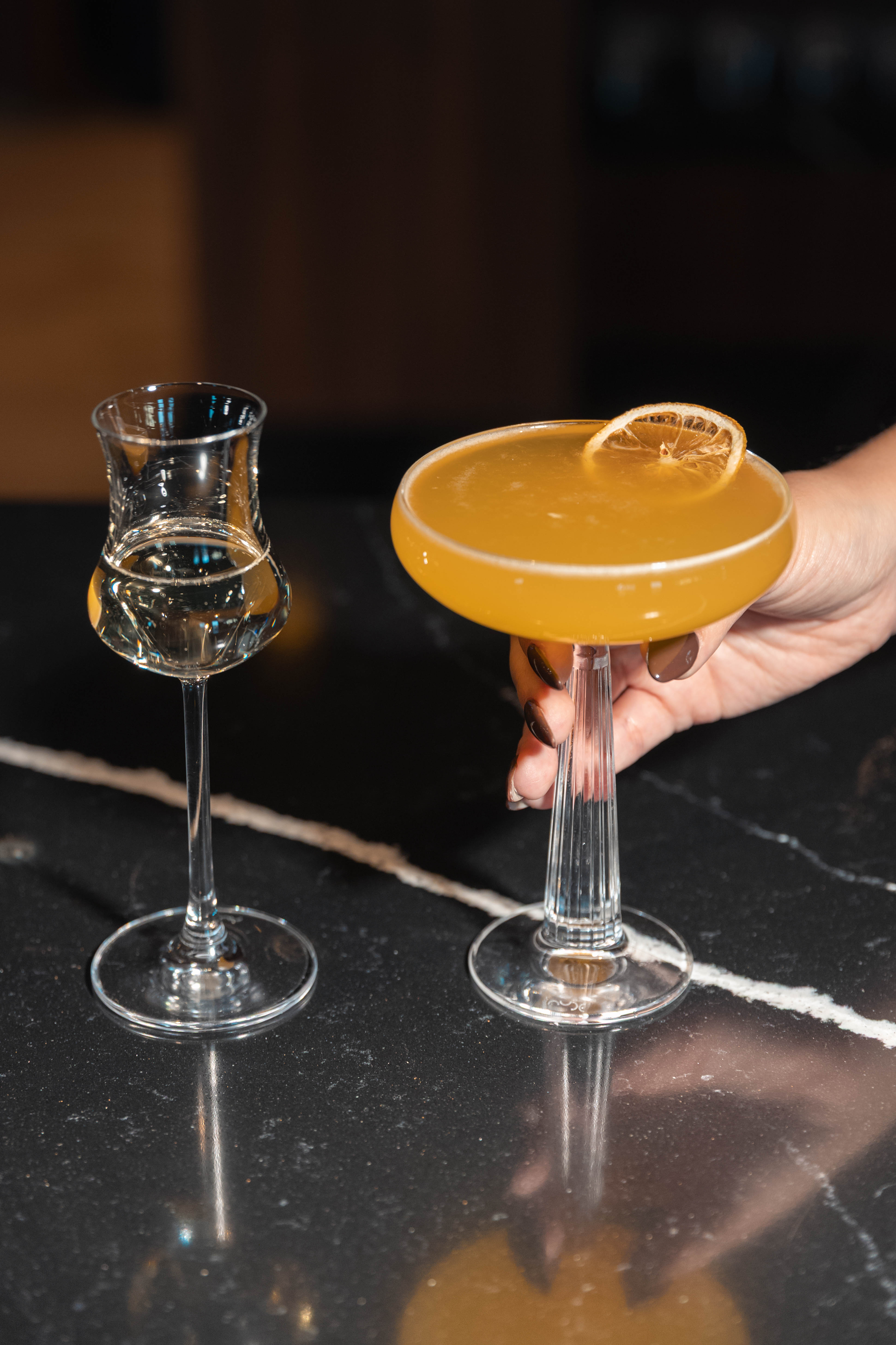 a hand holding a glass of yellow liquid next to a glass of yellow liquid