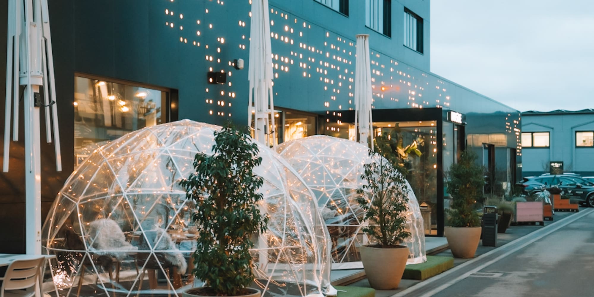 Modern restaurant patio with illuminated clear geodesic dining domes and plants.