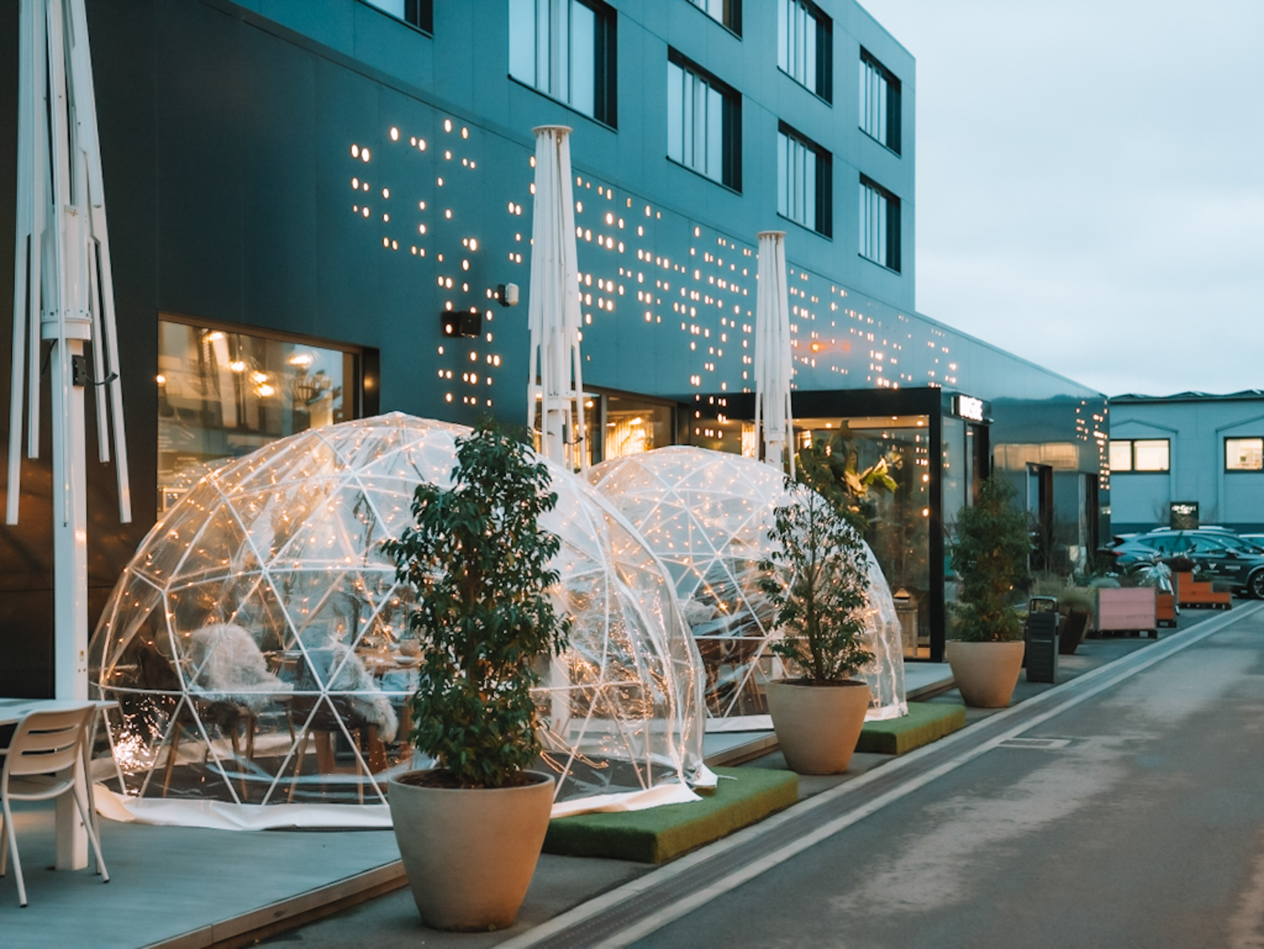 Modern restaurant patio with illuminated clear geodesic dining domes and plants.
