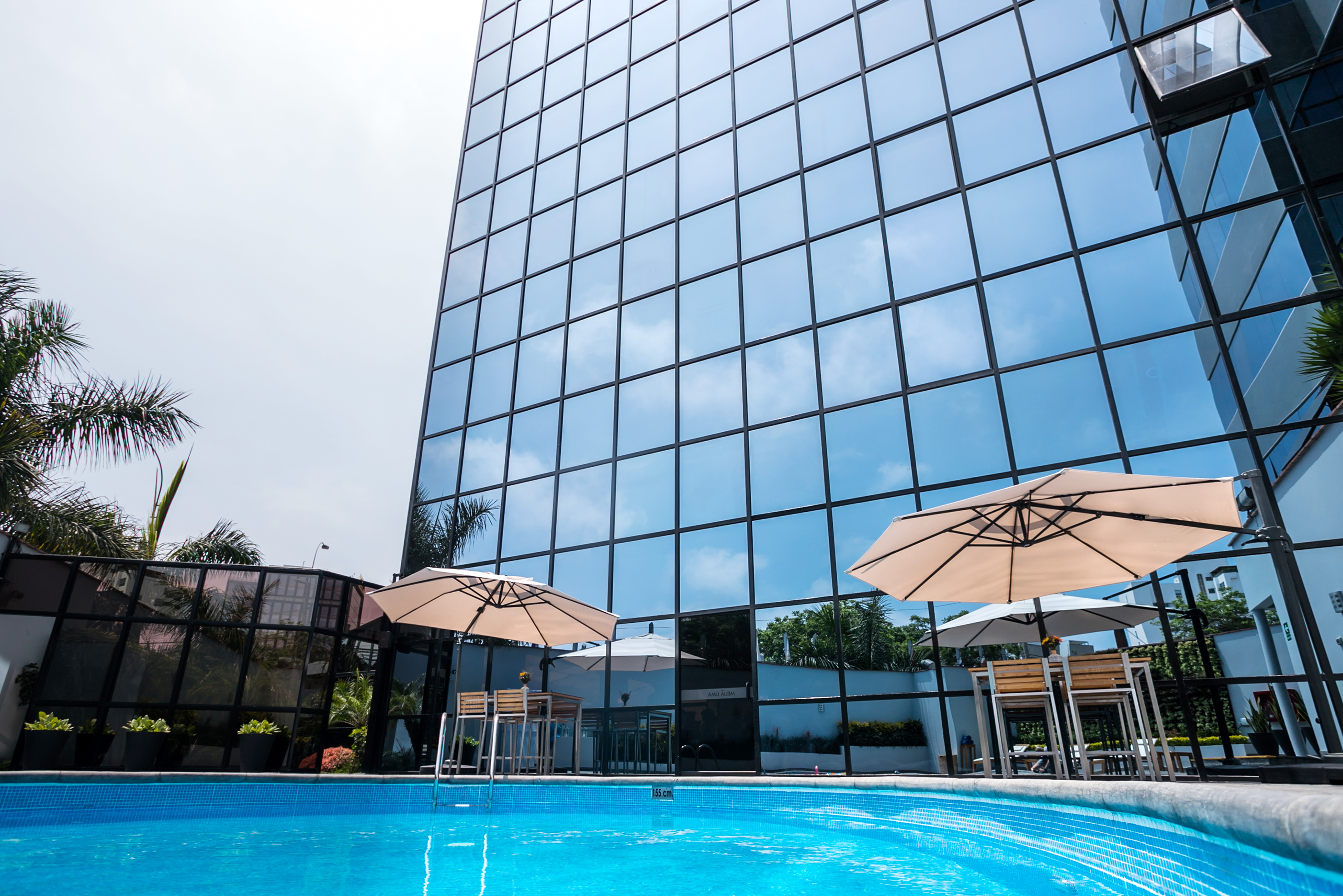 Modern glass hotel building with blue swimming pool and patio umbrellas.
