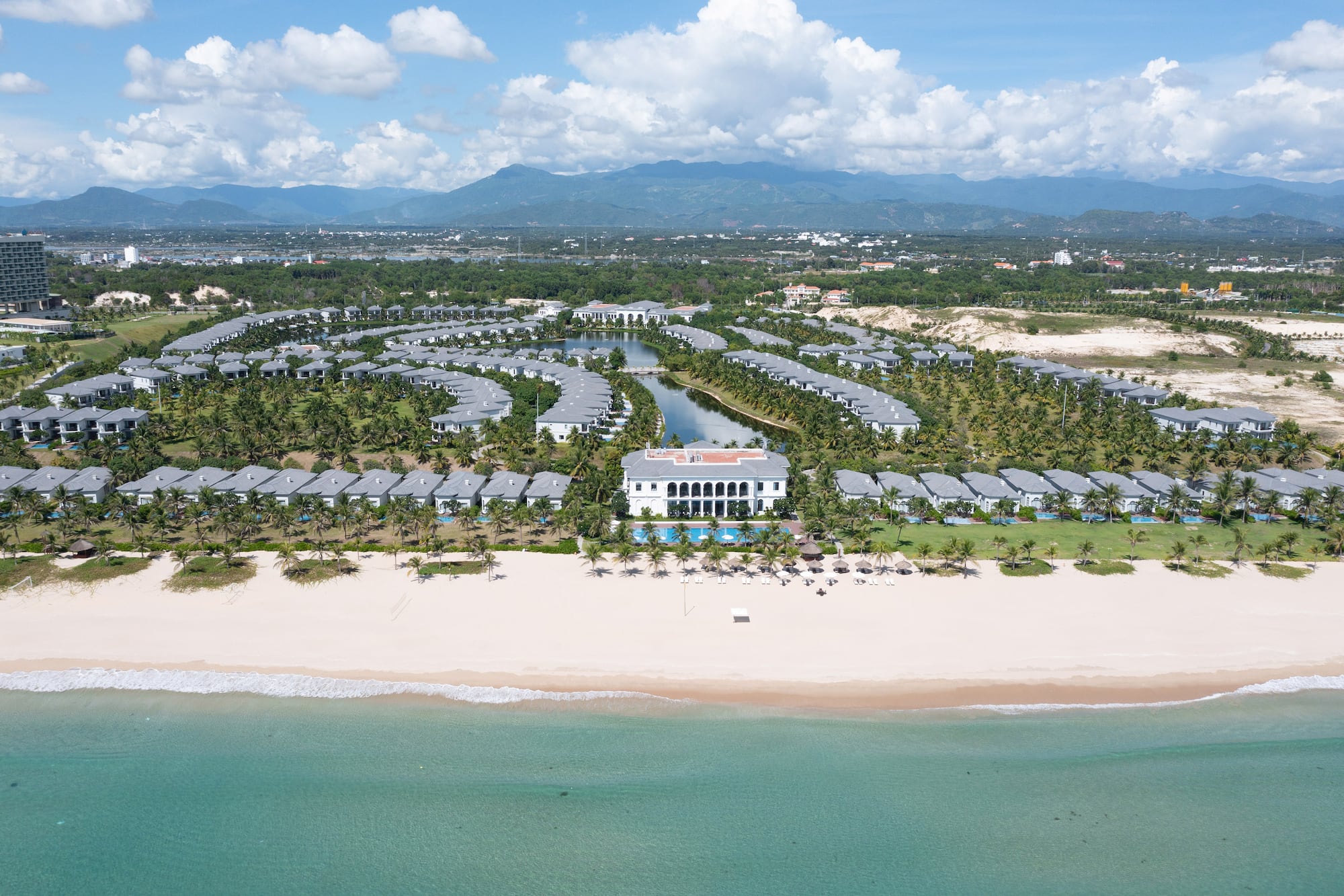 Tropical beach resort with luxury villas, pools, sandy shore, and blue ocean.