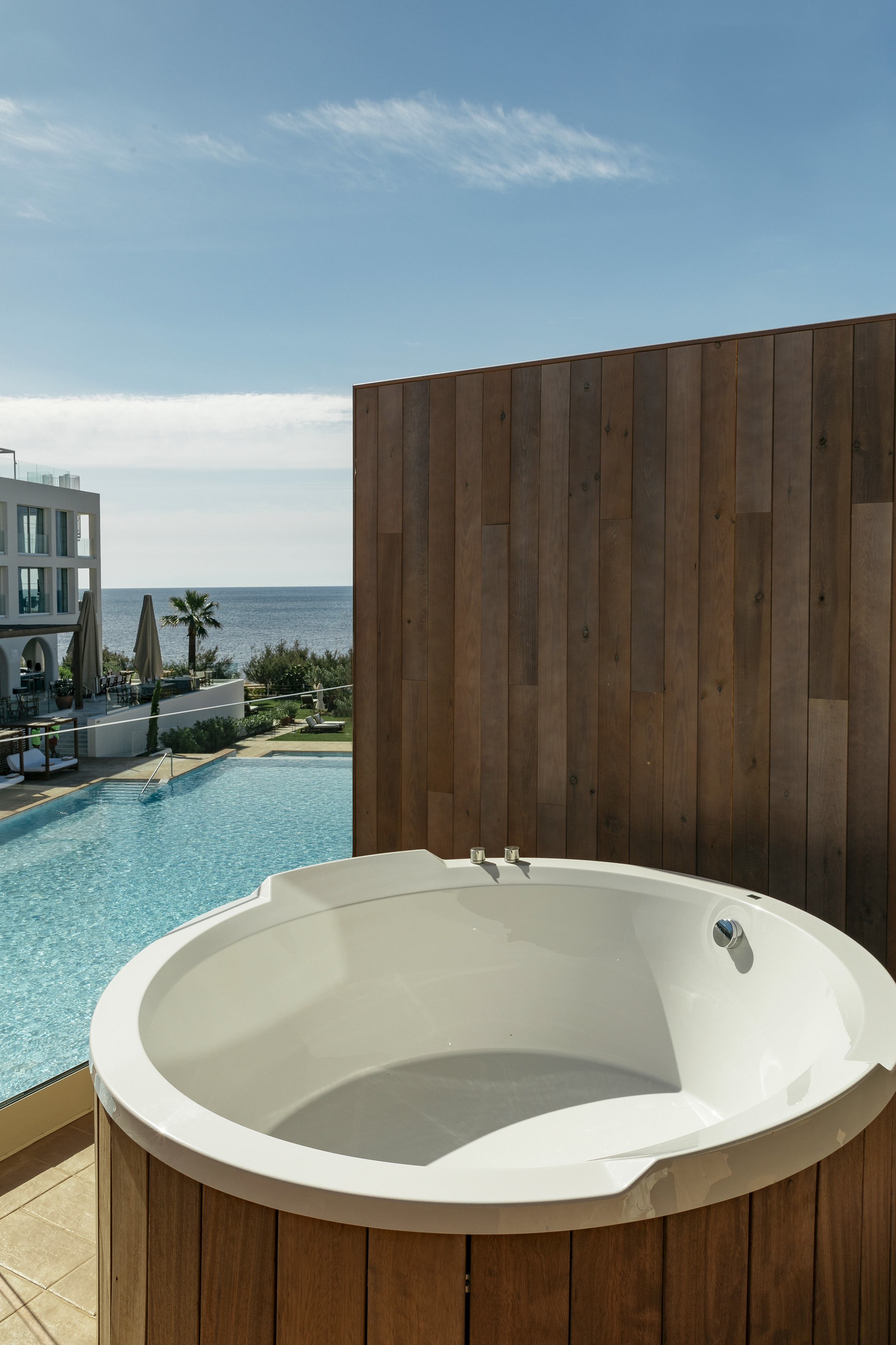 White outdoor jacuzzi, wooden exterior, resort pool, and ocean view.