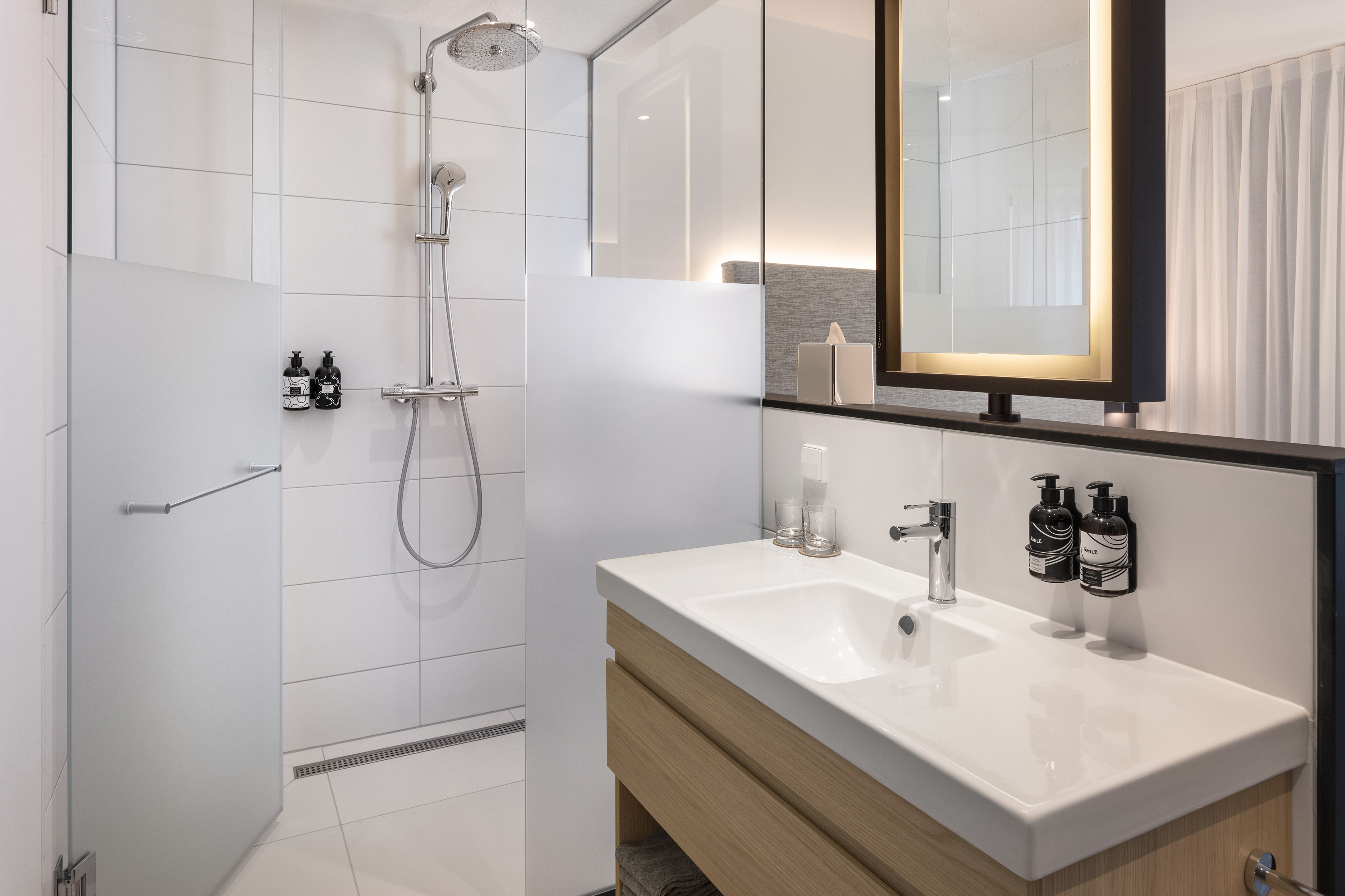 Modern white bathroom with glass shower, floating vanity, and illuminated mirror.