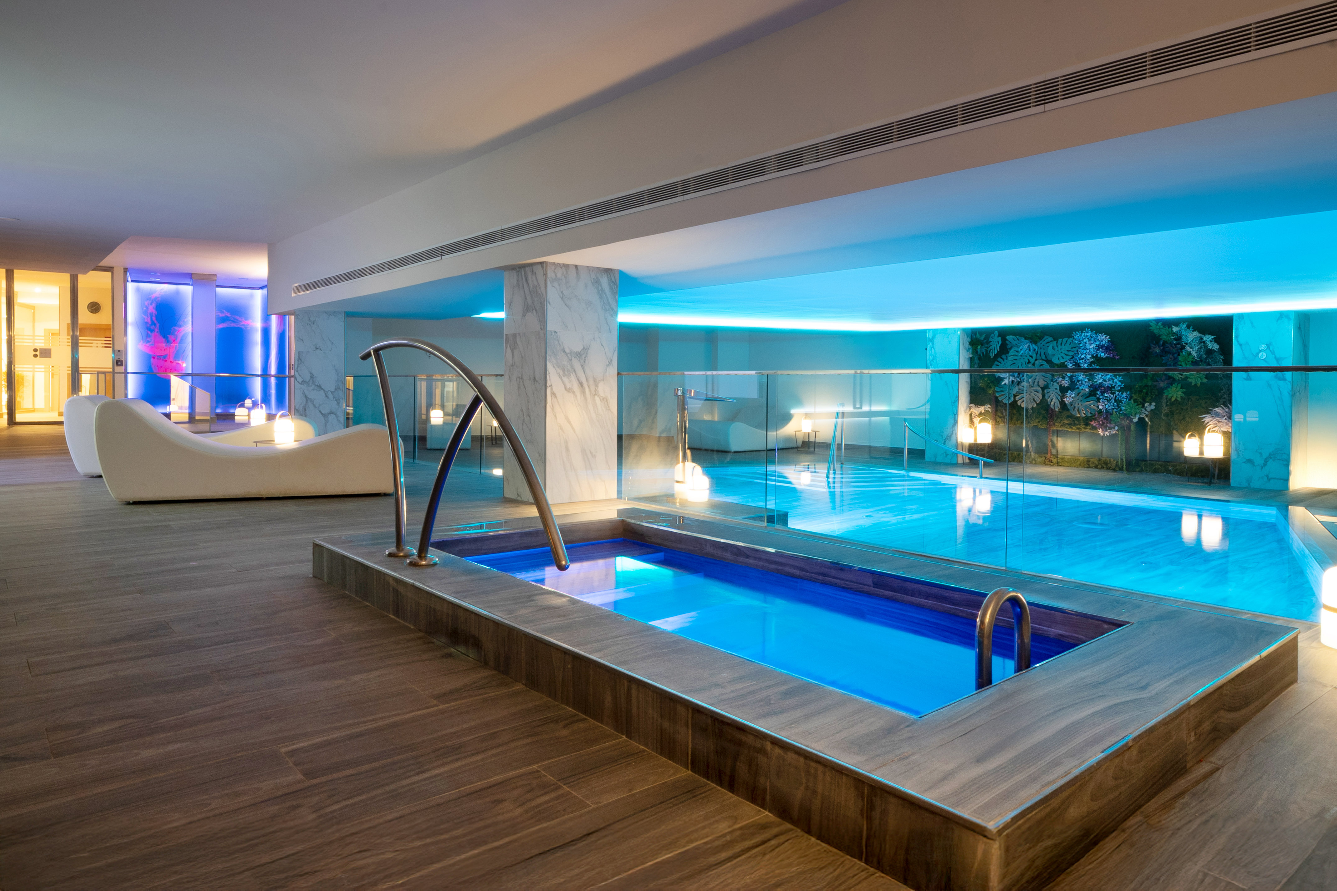 Luxurious indoor spa with blue-lit swimming pool, hot tub, and modern lounge area.