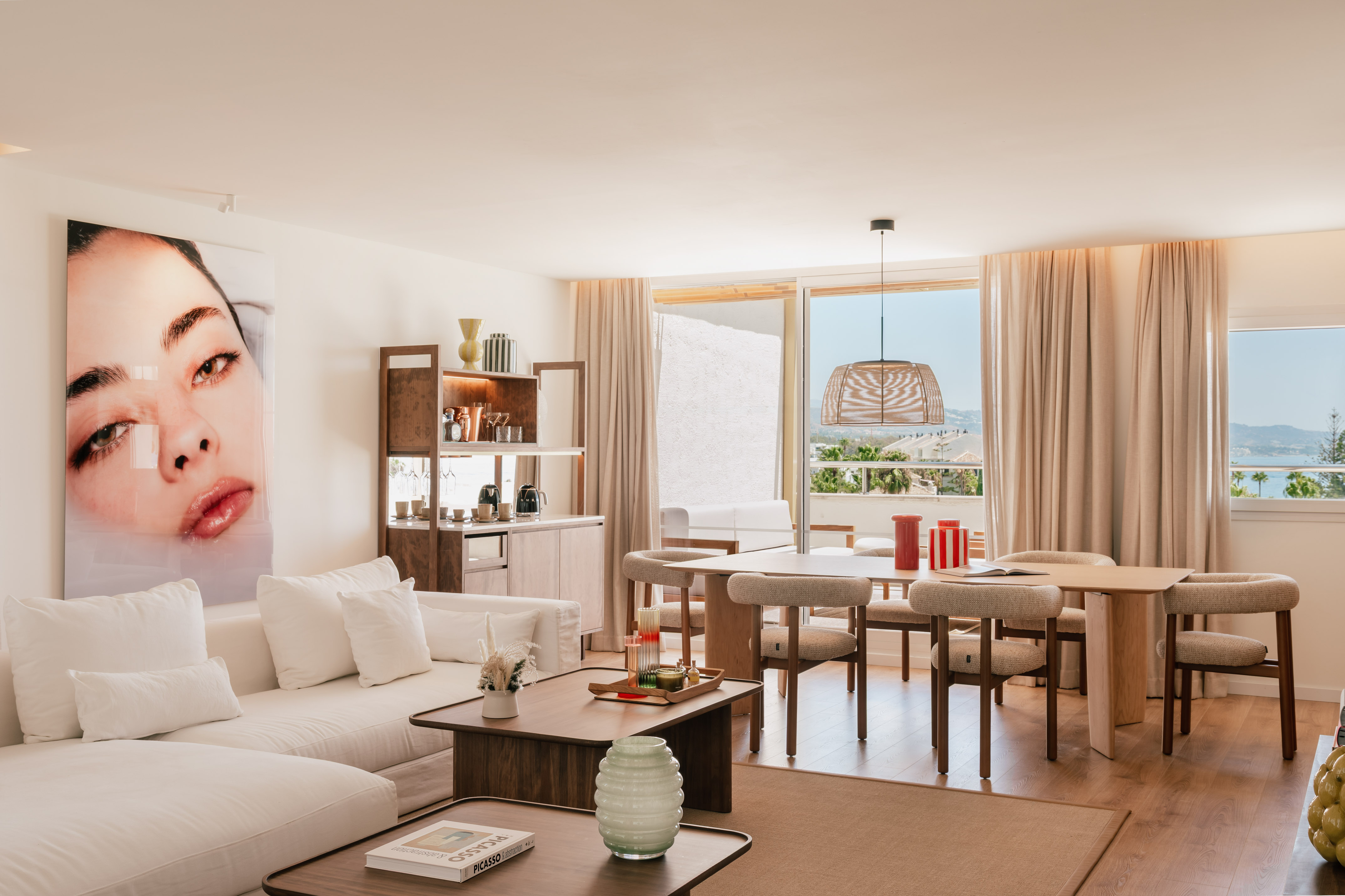 Modern living and dining room with ocean view, white sofa, and wood table.