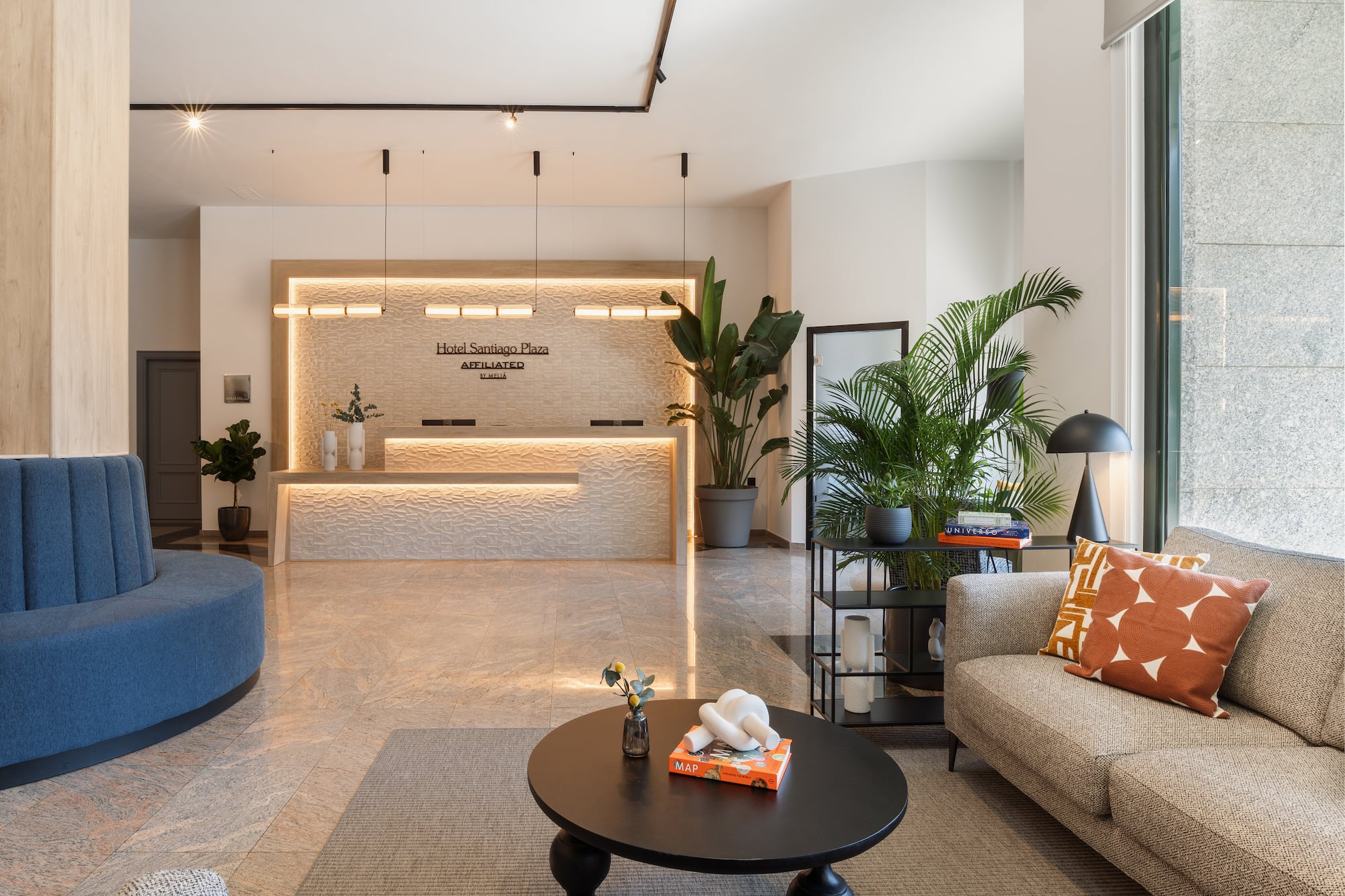 Modern hotel Santiago Plaza lobby with reception desk, blue and beige sofas, and plants.