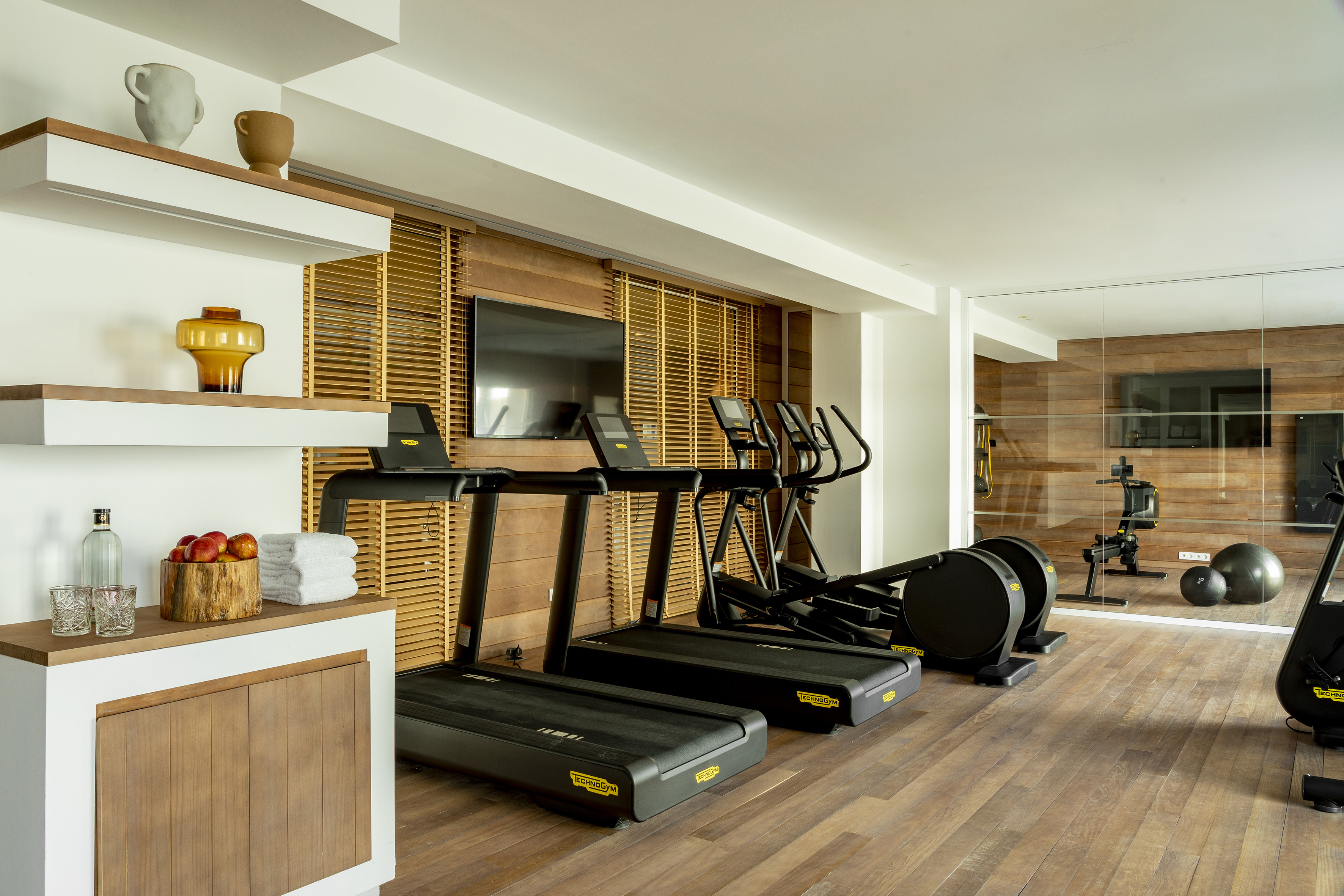 Modern home gym with treadmills, elliptical, wooden floor and wall.