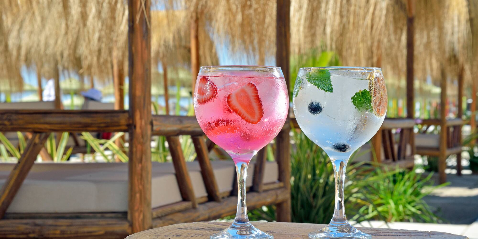 Strawberry and blueberry cocktails on wood table, beach bar background.