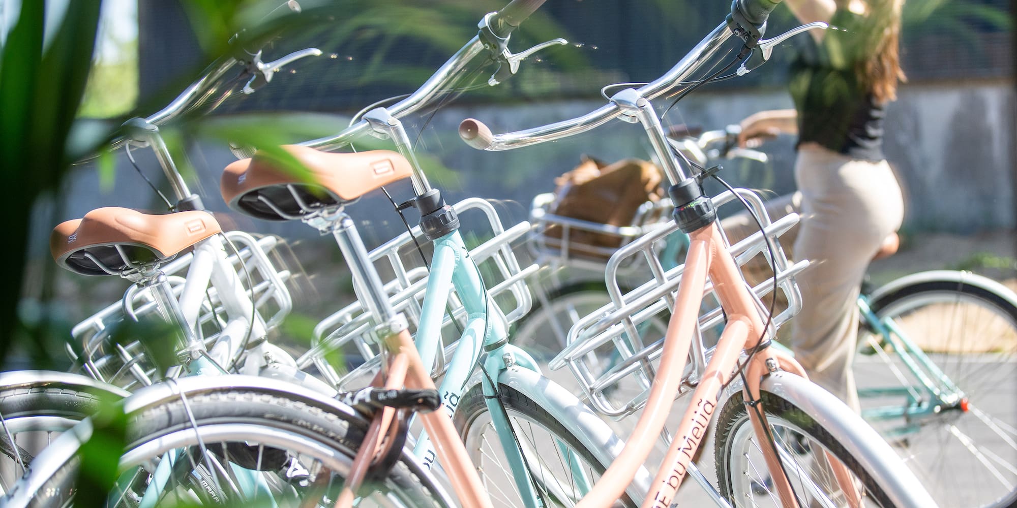INSIDE by Meliá pastel bikes with baskets and brown seats, amidst greenery.