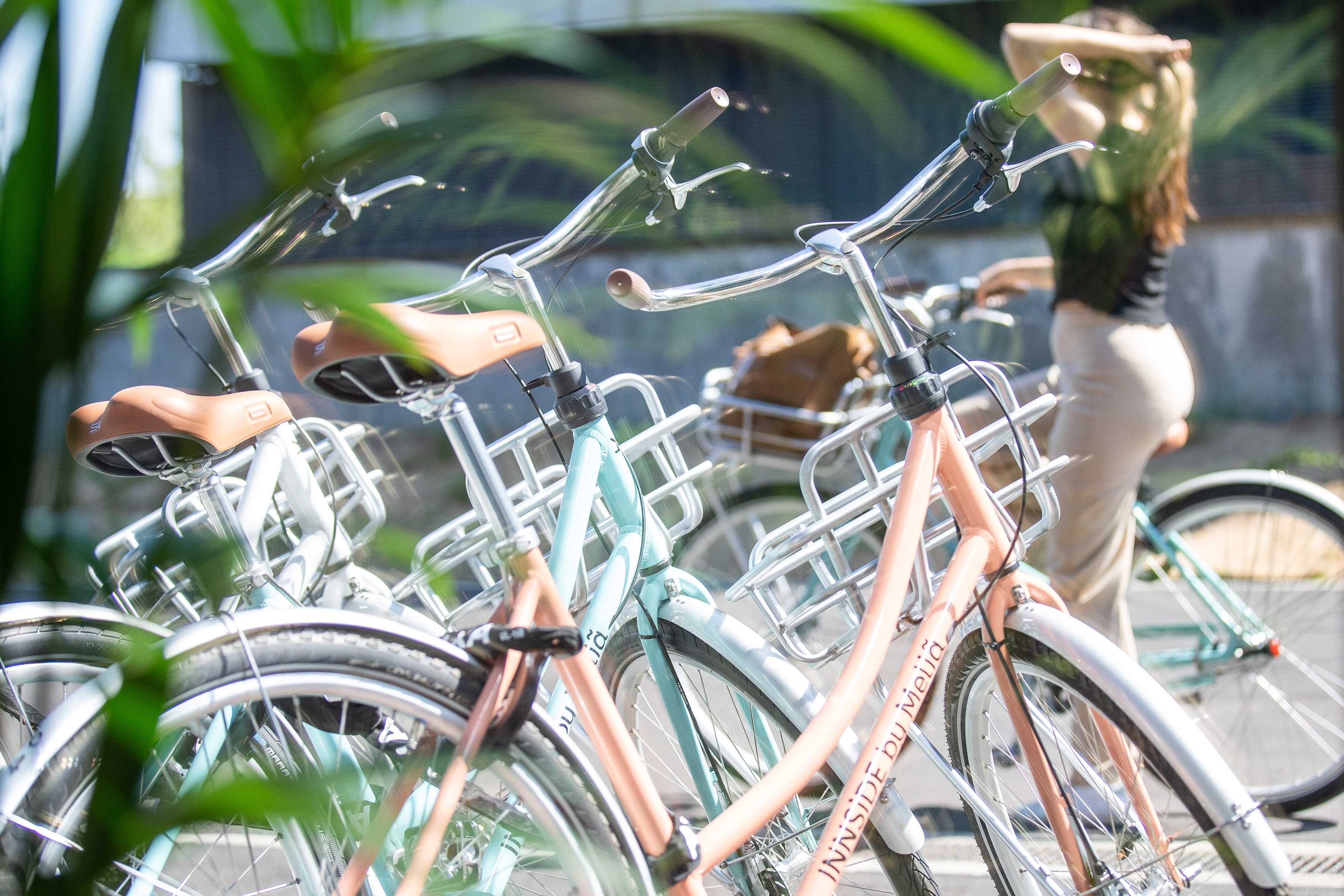 INSIDE by Meliá pastel bikes with baskets and brown seats, amidst greenery.