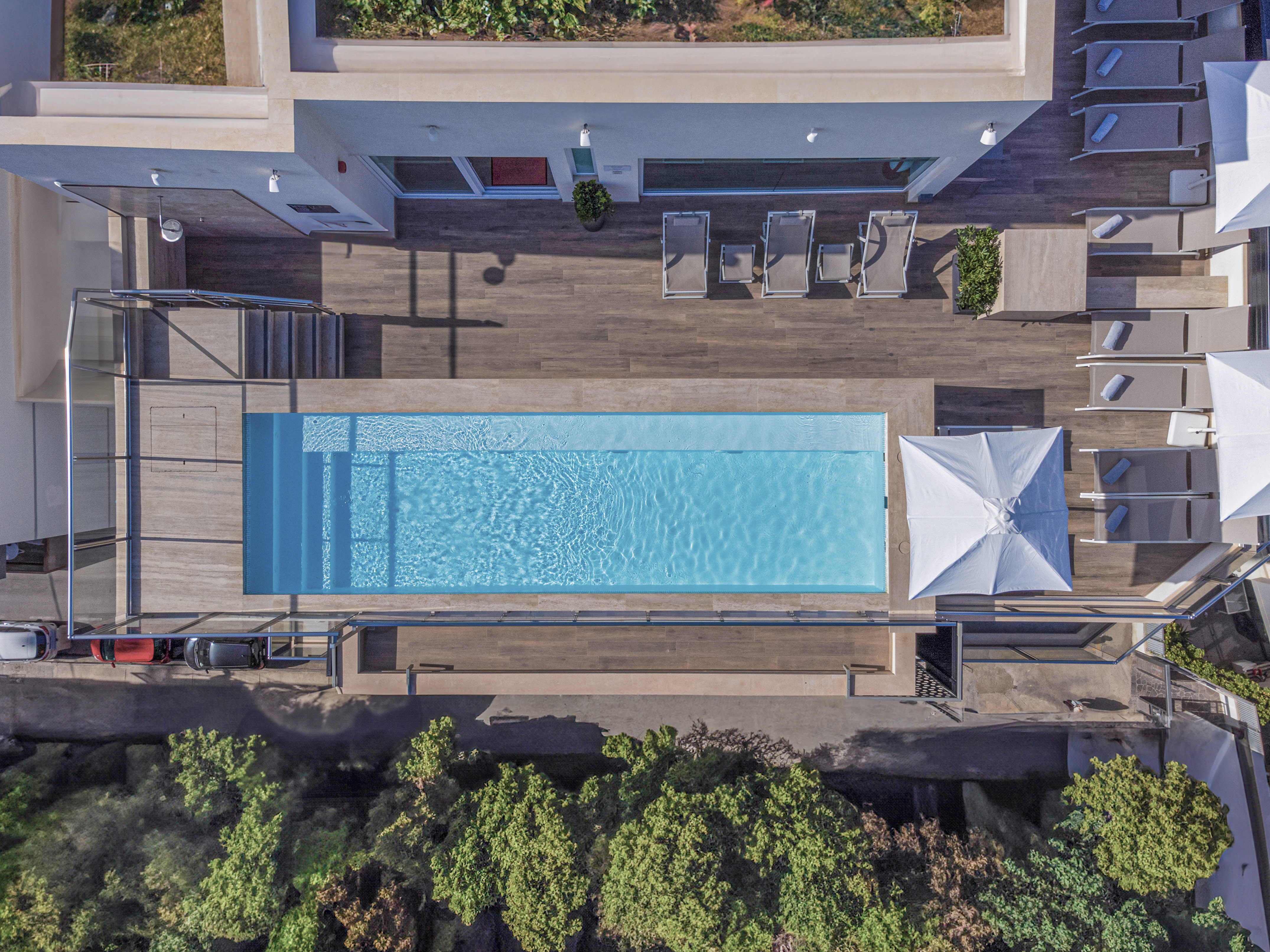 Aerial view of modern resort swimming pool, wooden deck, and sun loungers.