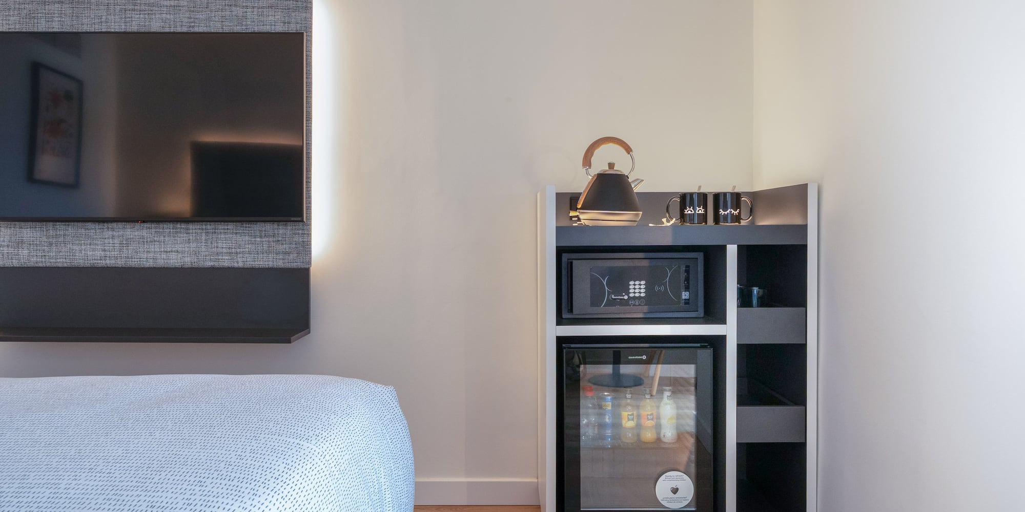 Habitación de hotel moderna con TV, minibar, caja fuerte y hervidor.