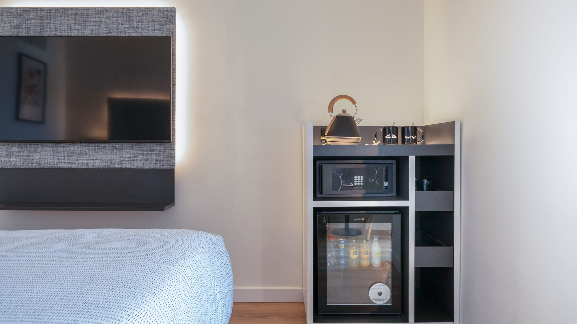 Habitación de hotel moderna con TV, minibar, caja fuerte y hervidor.