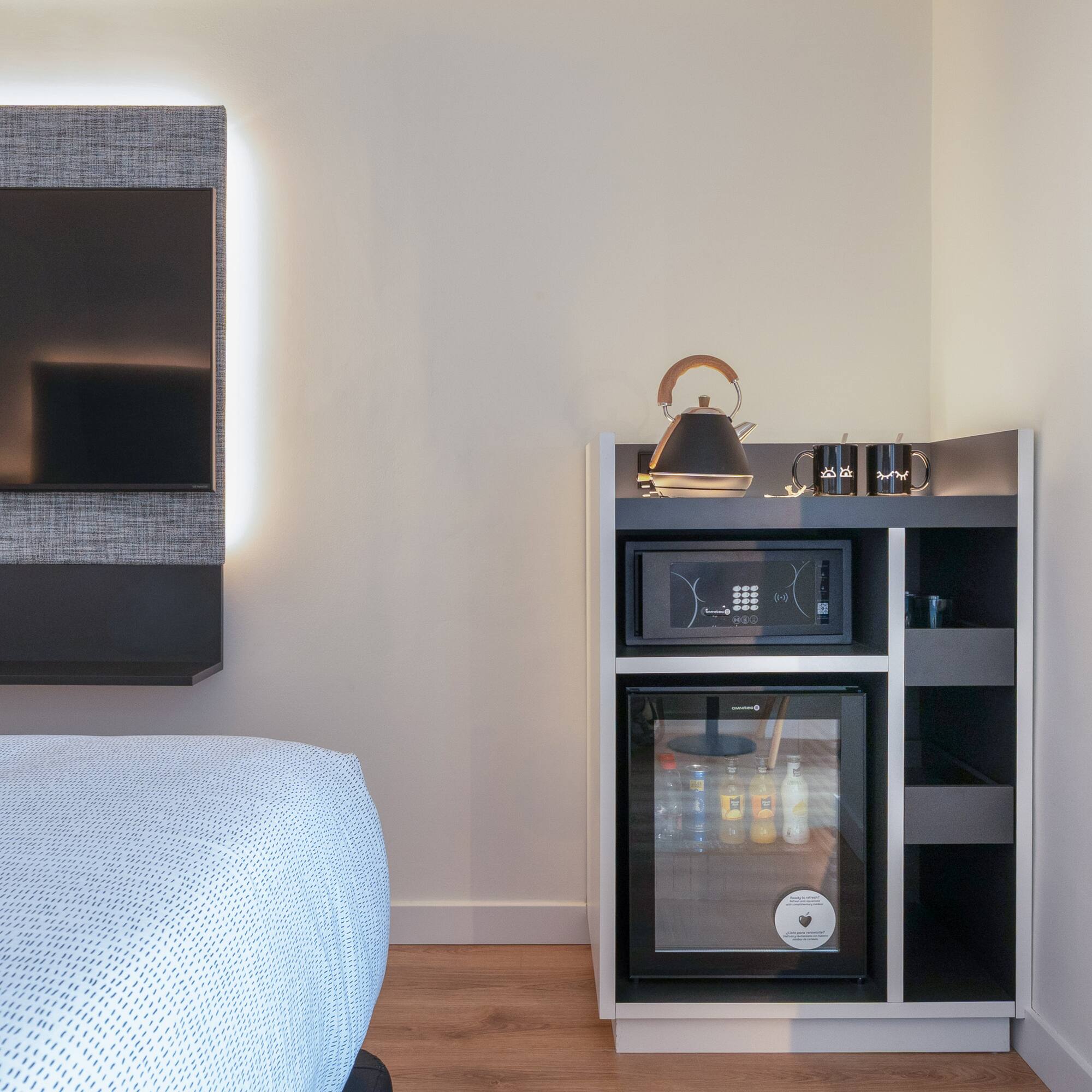 Habitación de hotel moderna con TV, minibar, caja fuerte y hervidor.