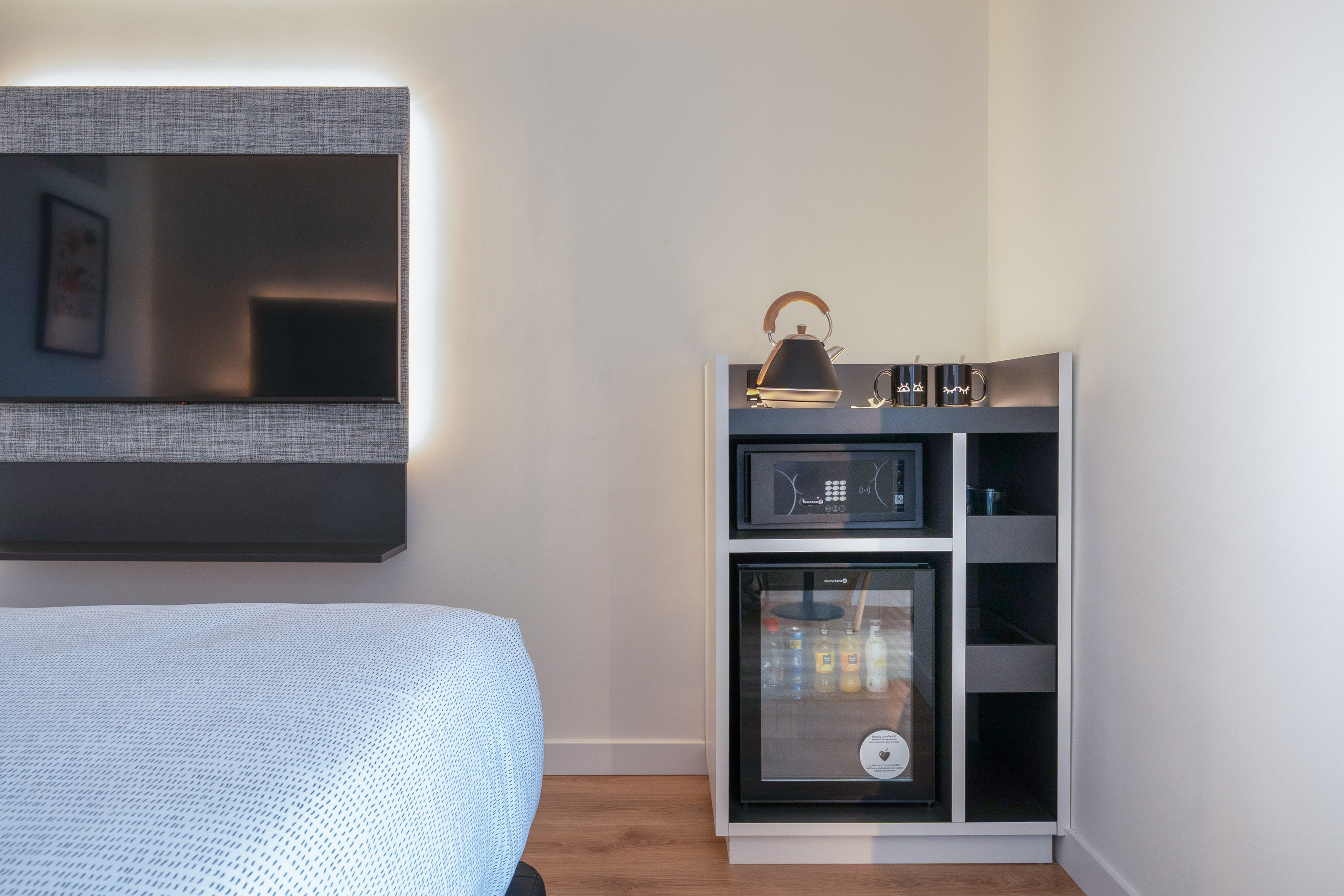 Habitación de hotel moderna con TV, minibar, caja fuerte y hervidor.