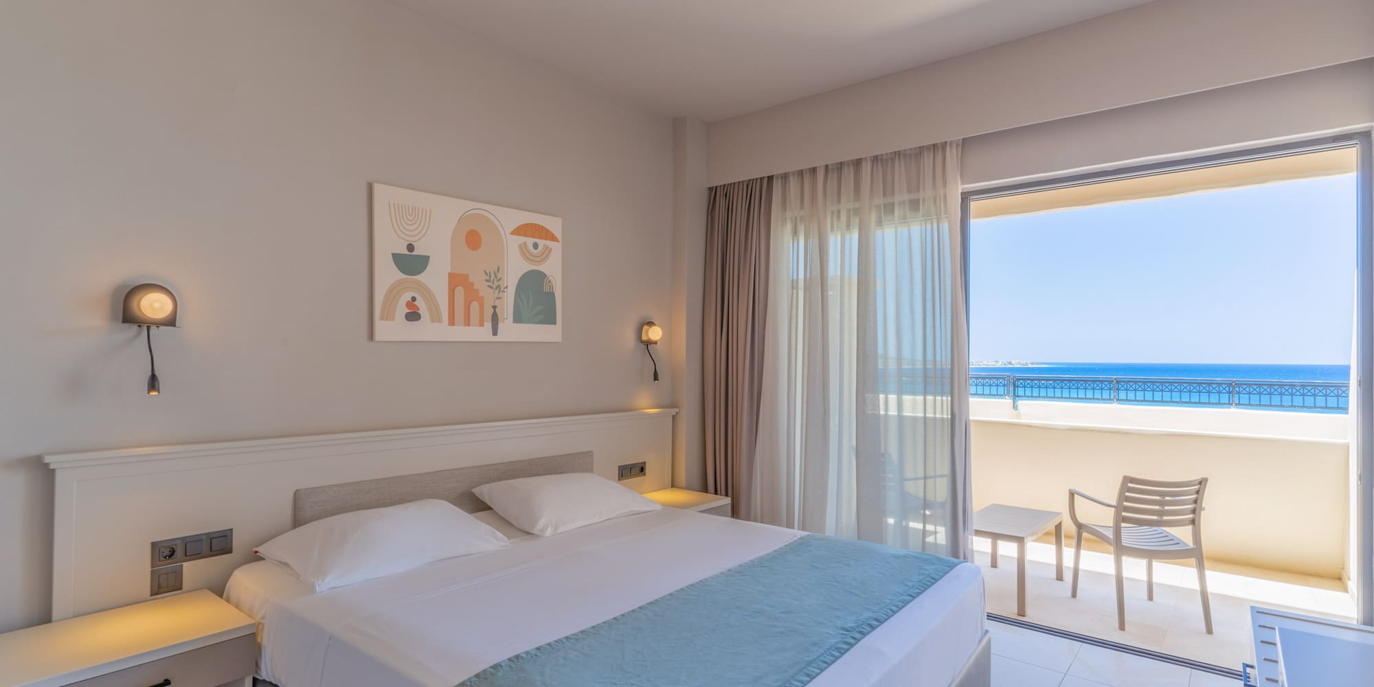 Bright hotel room with double bed, modern decor, and ocean view balcony.