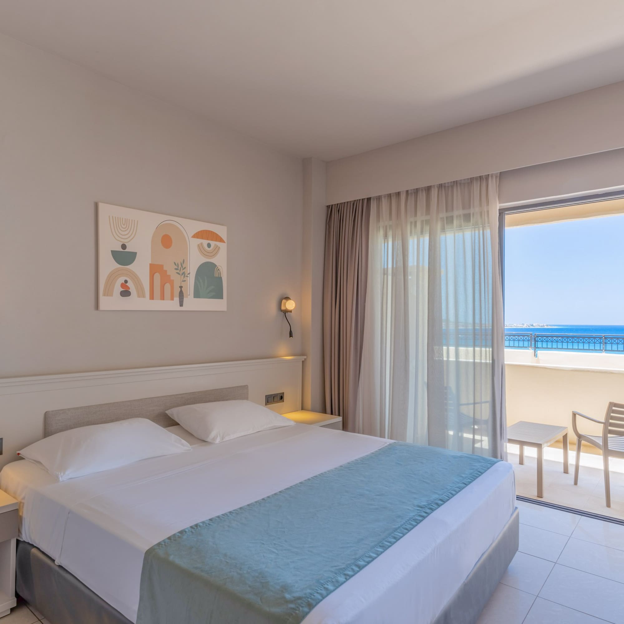 Bright hotel room with double bed, modern decor, and ocean view balcony.