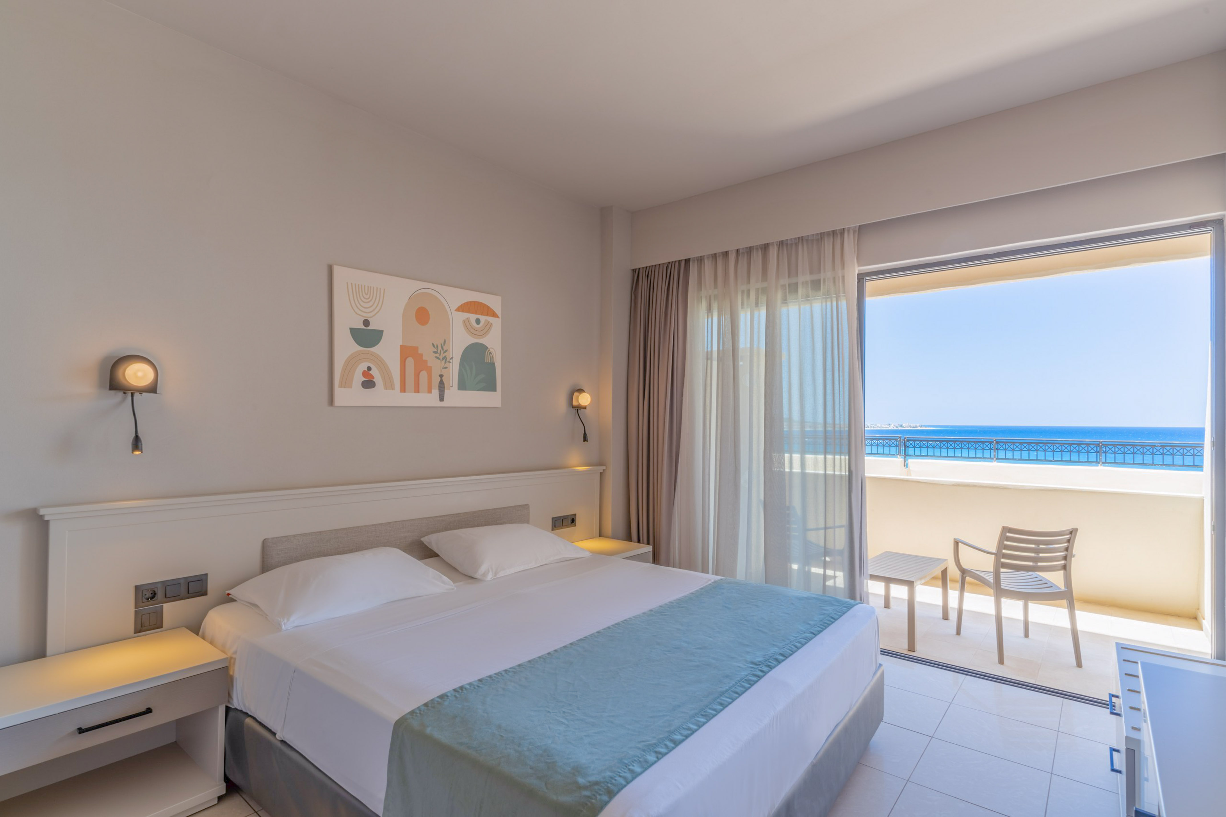 Bright hotel room with double bed, modern decor, and ocean view balcony.