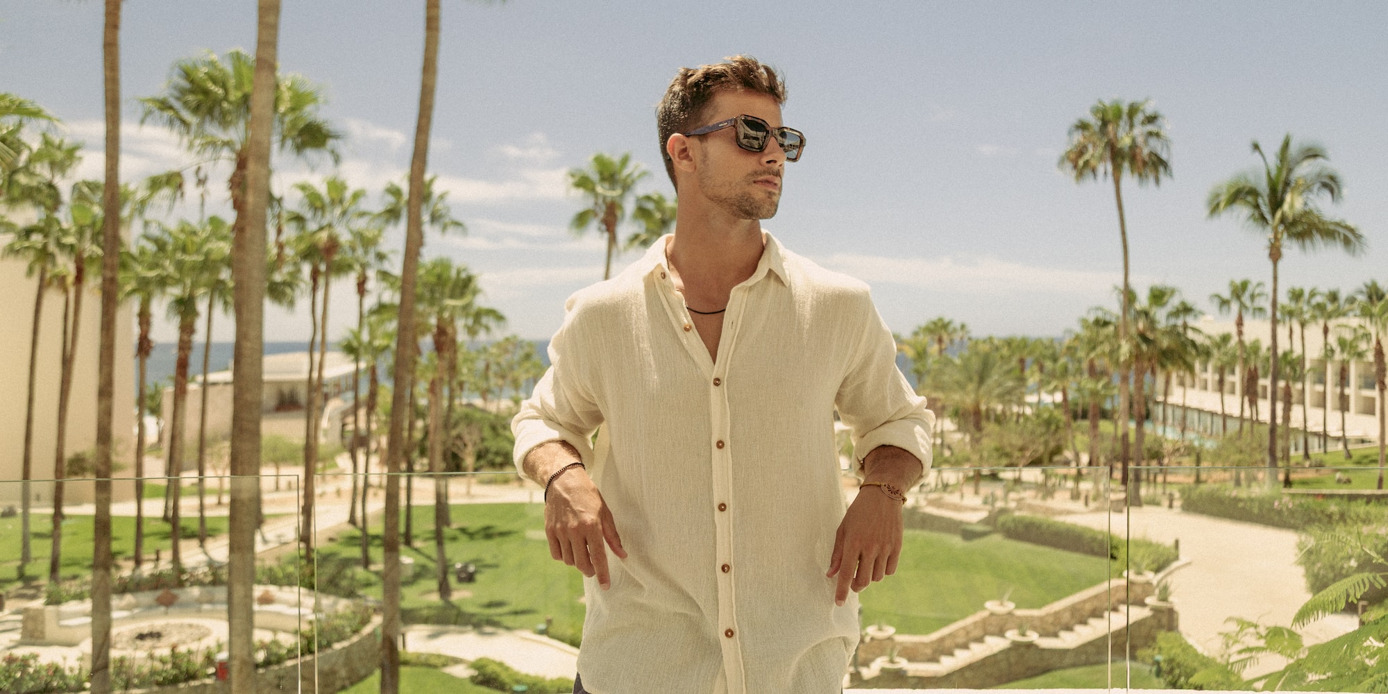 a man standing on a balcony with palm trees