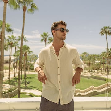 a man standing on a balcony with palm trees