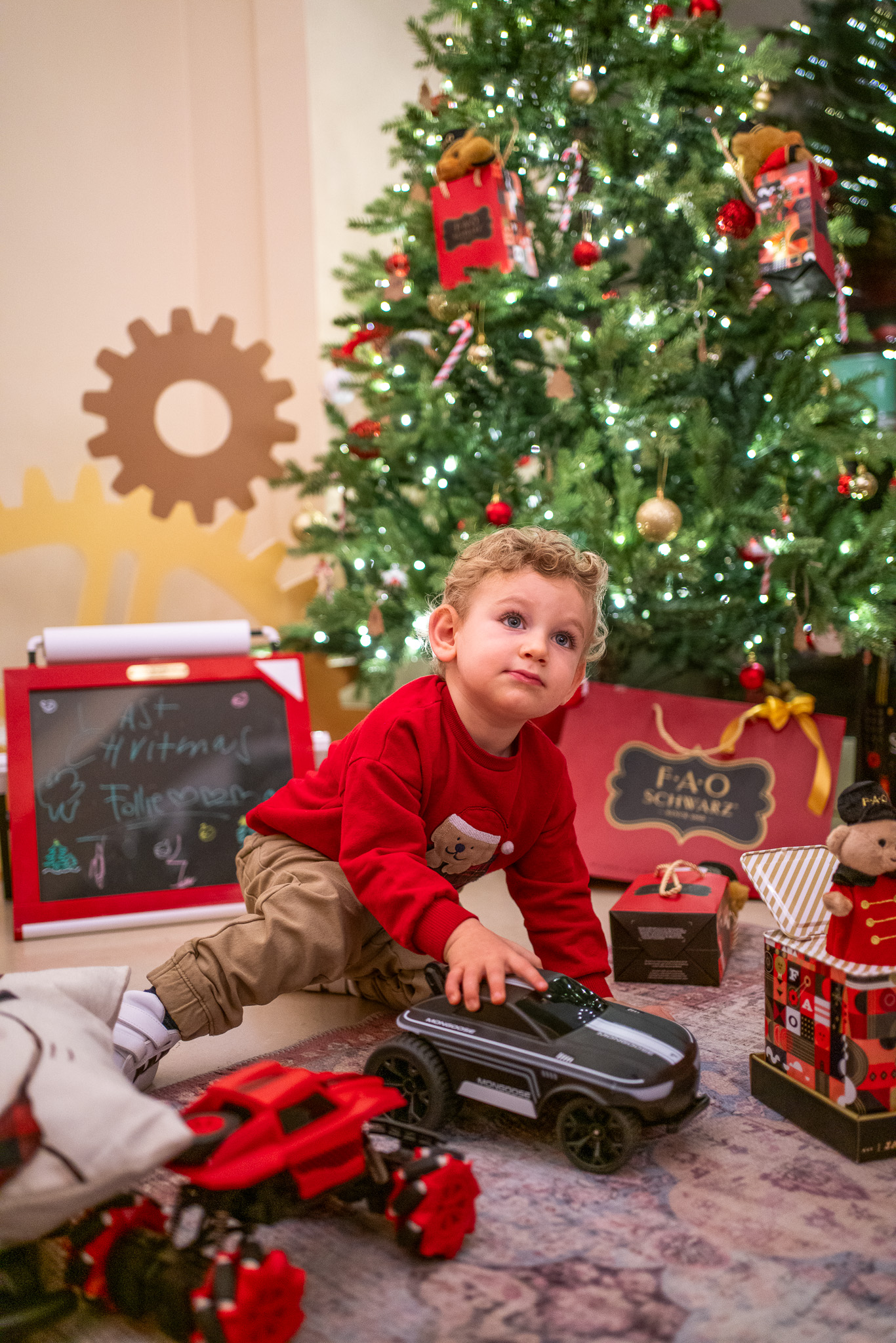 Young boy plays with toy cars by Christmas tree and FAO Schwarz gifts.