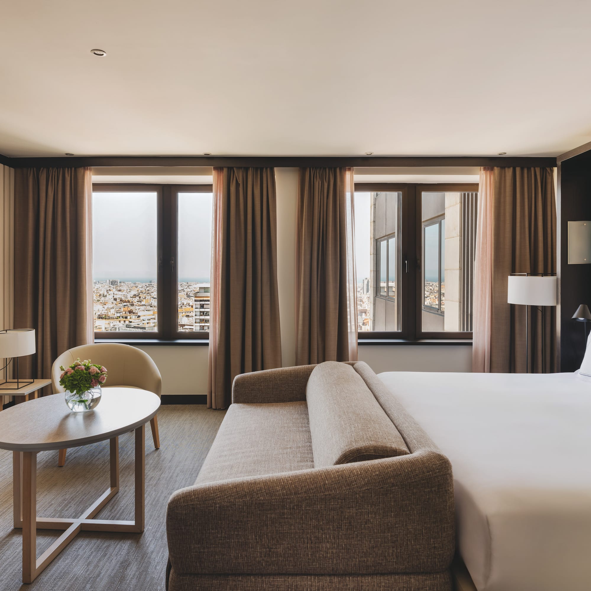 Habitación de hotel con cama, sofá, mesa y vistas urbanas.