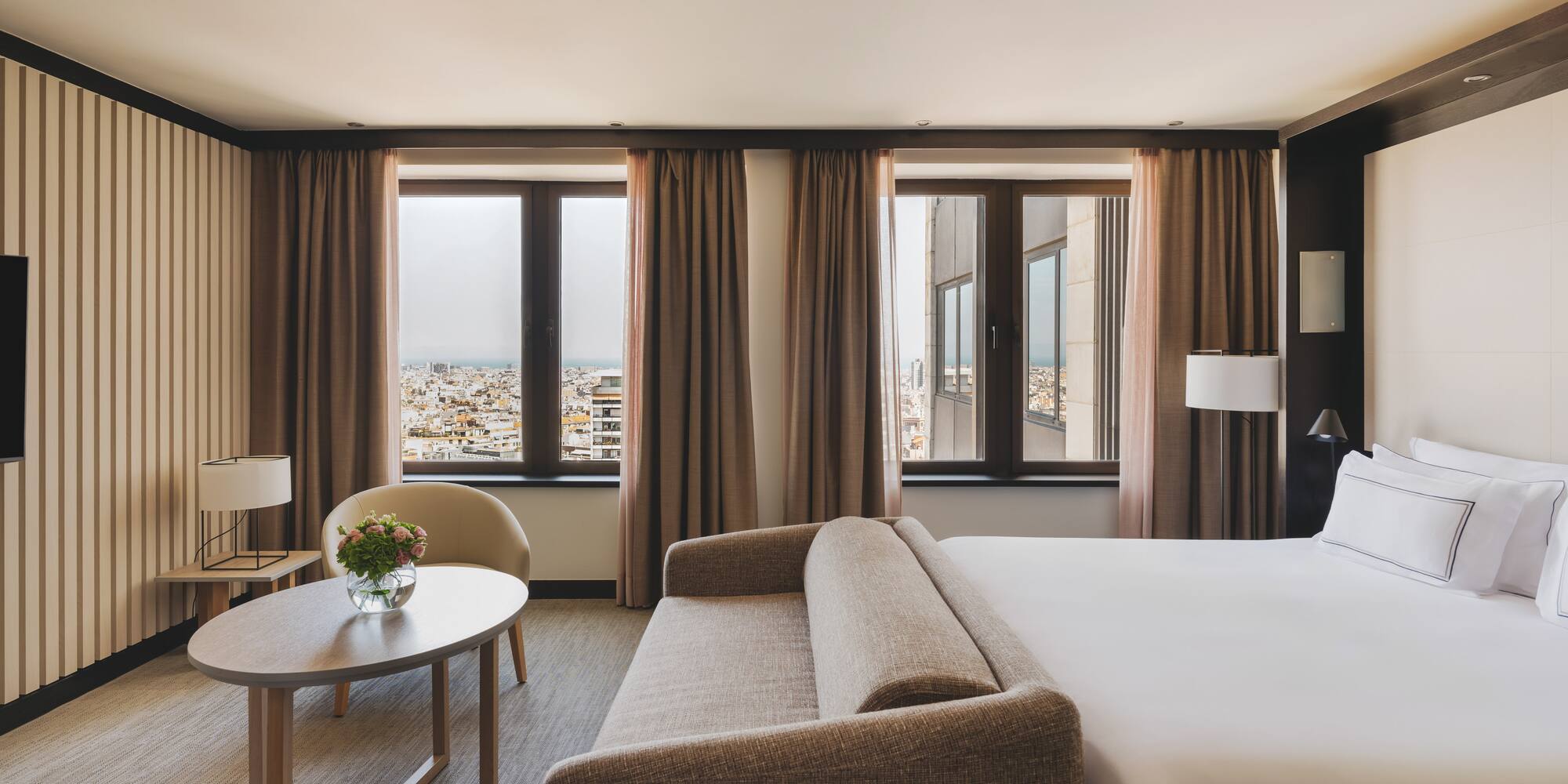 Habitación de hotel con cama, sofá, mesa y vistas urbanas.