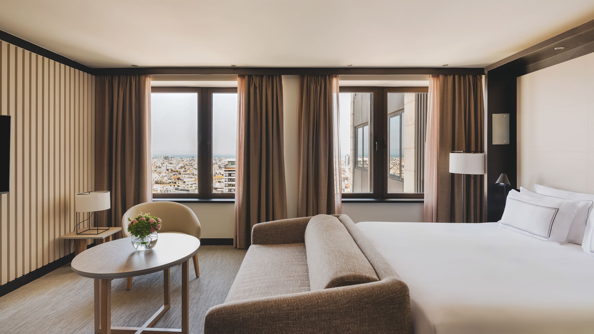 Habitación de hotel con cama, sofá, mesa y vistas urbanas.