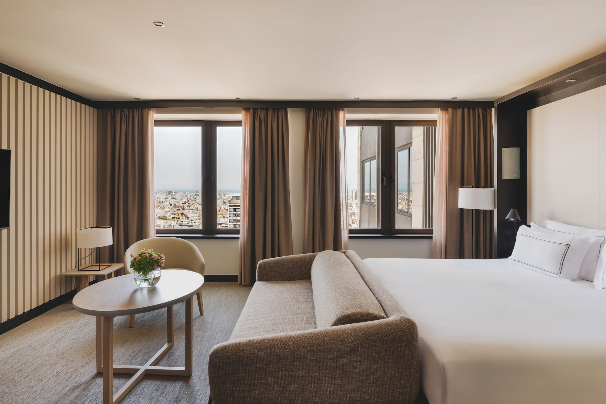Habitación de hotel con cama, sofá, mesa y vistas urbanas.