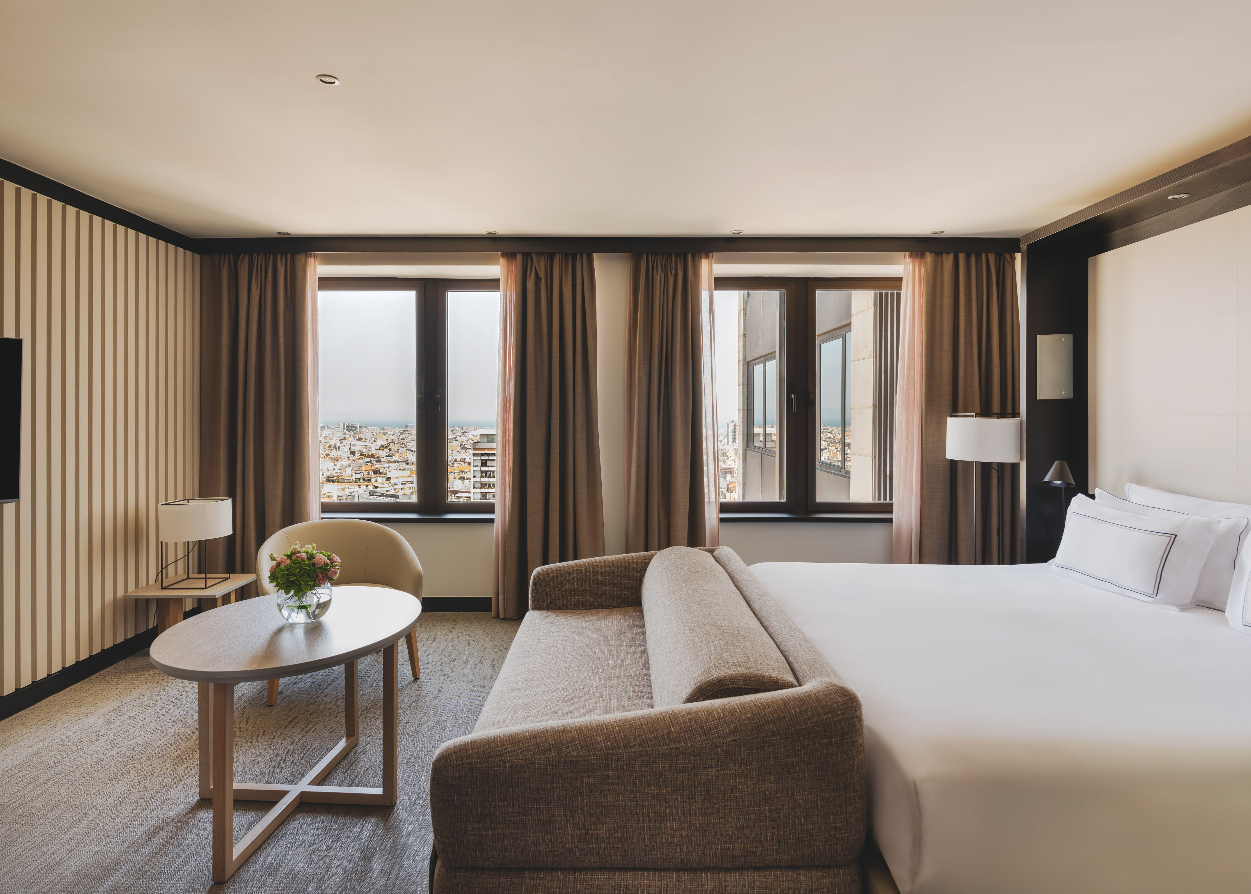 Habitación de hotel con cama, sofá, mesa y vistas urbanas.
