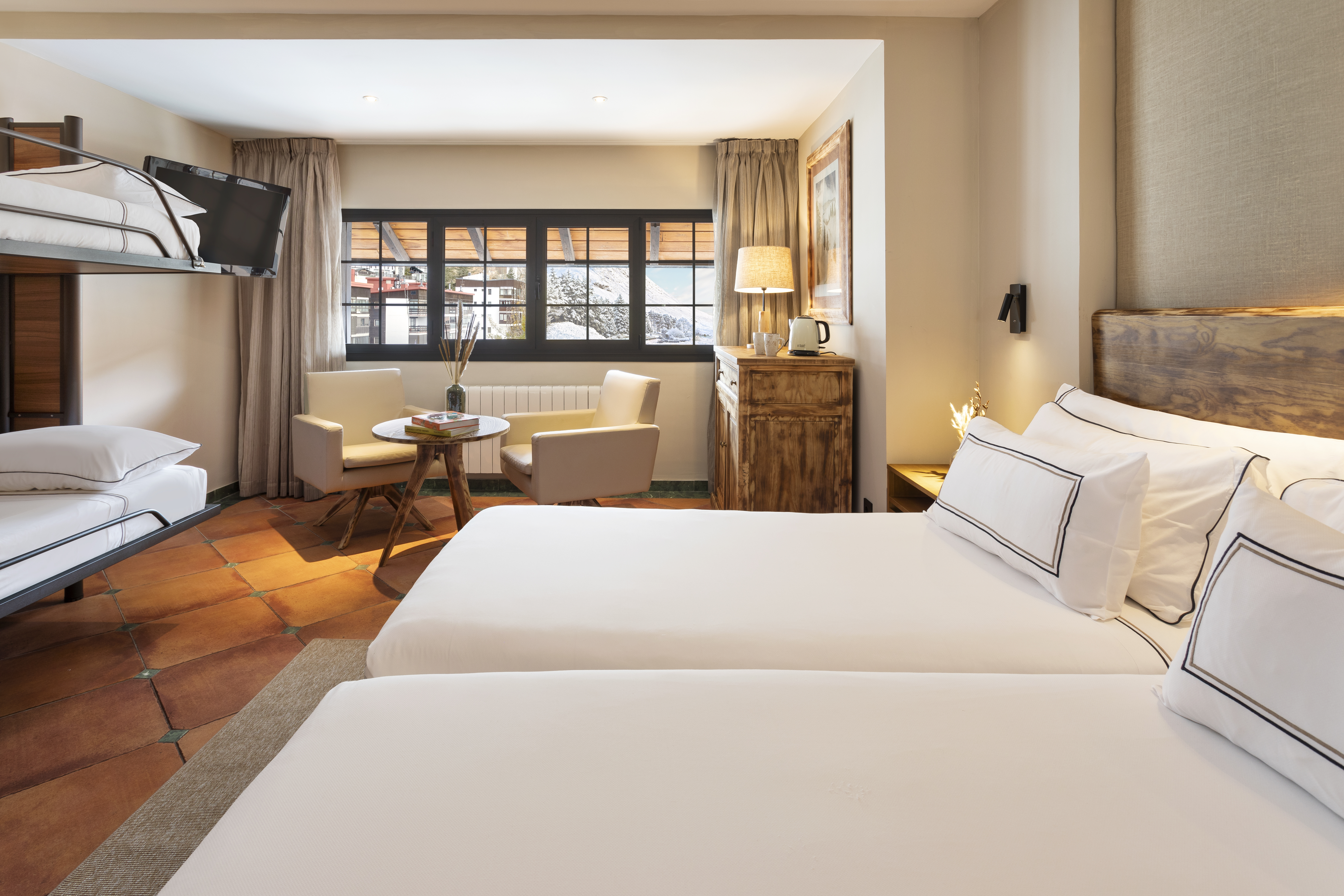 Cozy hotel room with twin beds, bunk bed, terracotta floor, mountain view.